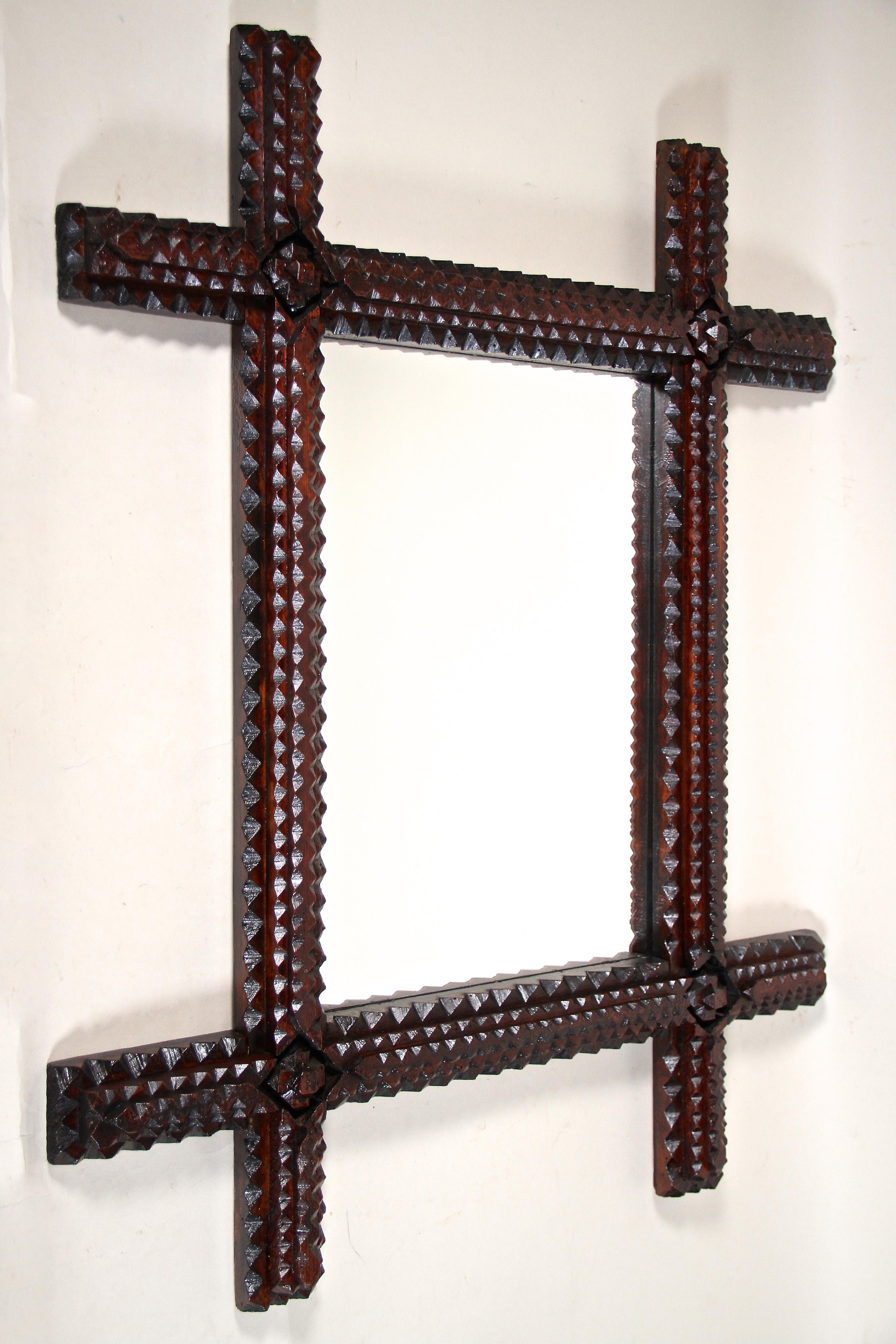 Unusual rustic Tramp Art wall mirror from the late 19th century around 1870 in Austria. Hand carved out of fine basswood, the wide frame shows a gorgeous chip carved design with spectacular made corners. The very dark brown stained surface shows a