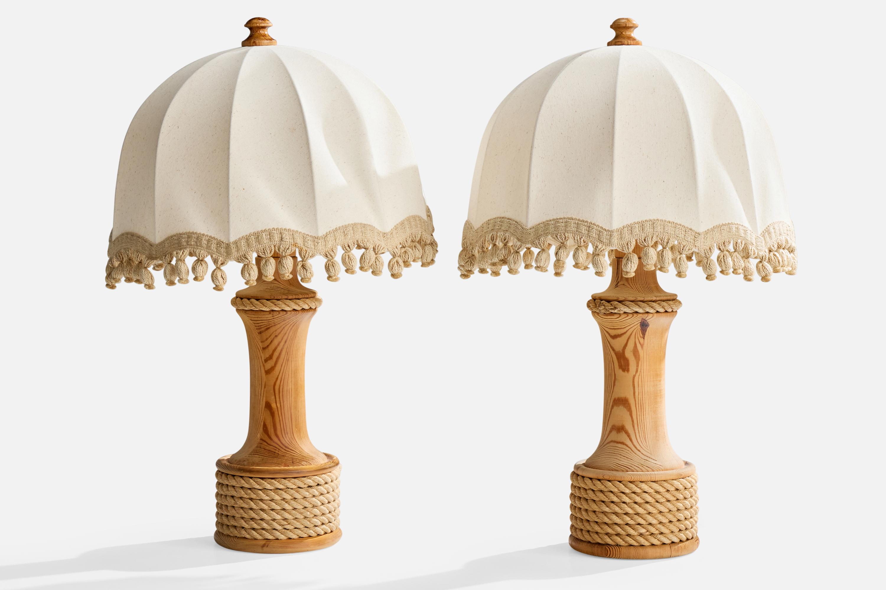 A pair of pine, rope and white fabric table lamps produced by Tranås Stilarmatur, Sweden, c. 1970s.

Dry crack to pine base as illustrated.

Wear to wood consistent with age and use

Vintage lampshades in fair condition

Wear consistent with age and