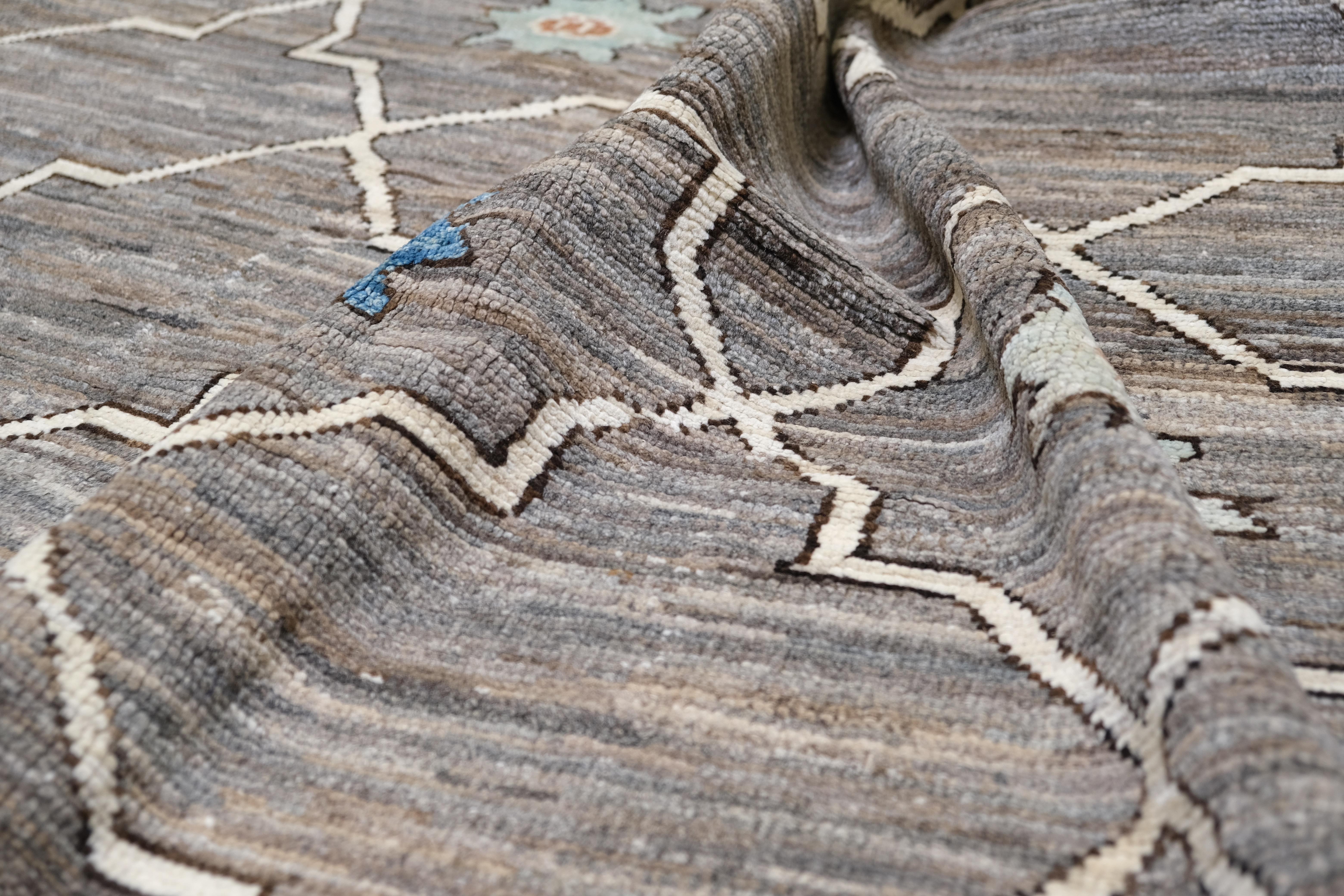 Ce magnifique tapis en laine nouée à la main au Pakistan allie un savoir-faire traditionnel à un design géométrique contemporain. Le motif en treillis complexe, mis en valeur par de charmants accents floraux dans des teintes douces de bleu, de