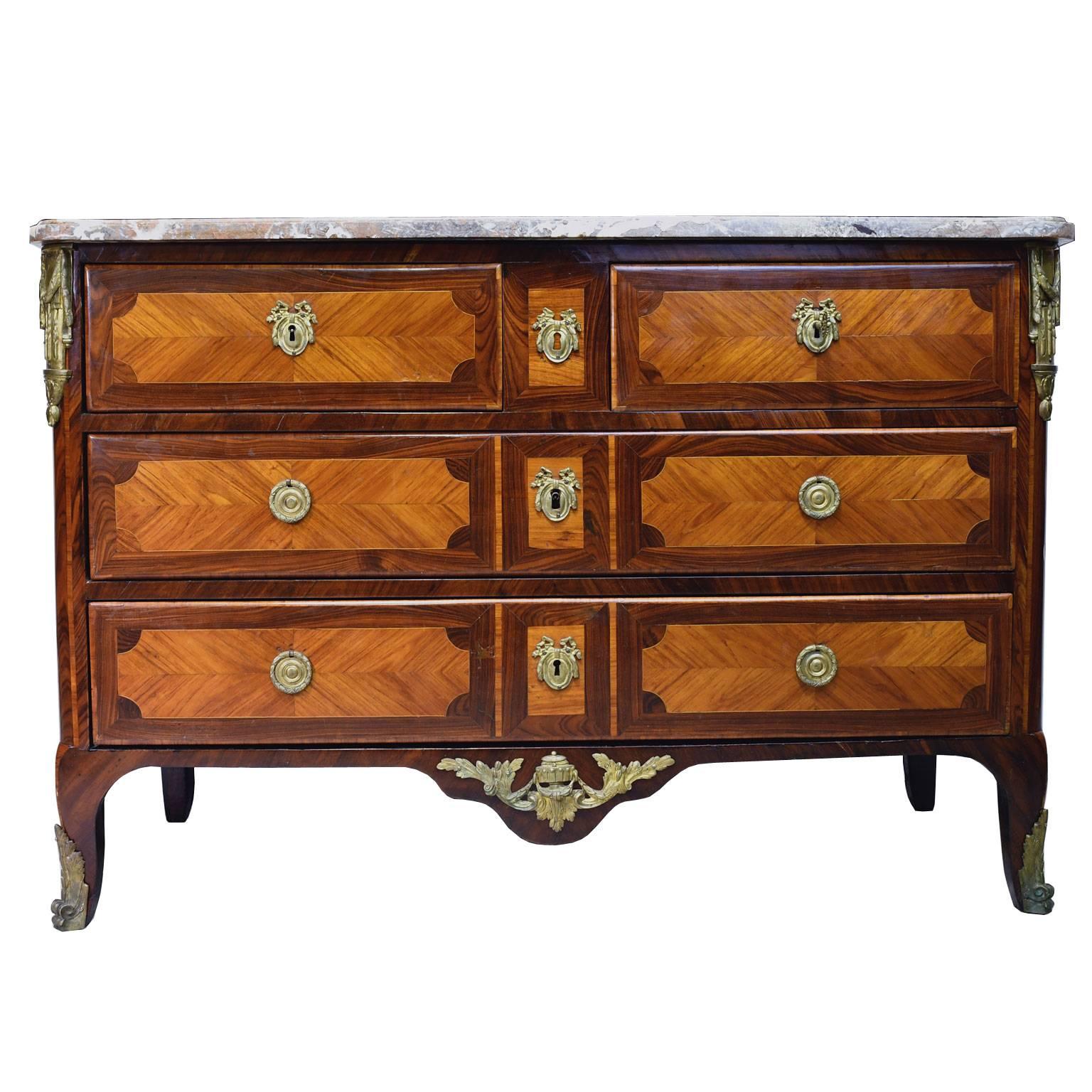 A stunning French commode with parquetry inlays in kingwood, rosewood and tulipwood, with bronze doré ormolu, original marble top and hardware. Chest is in a transitional form that references but departs from the rococo style of Louis XV, and