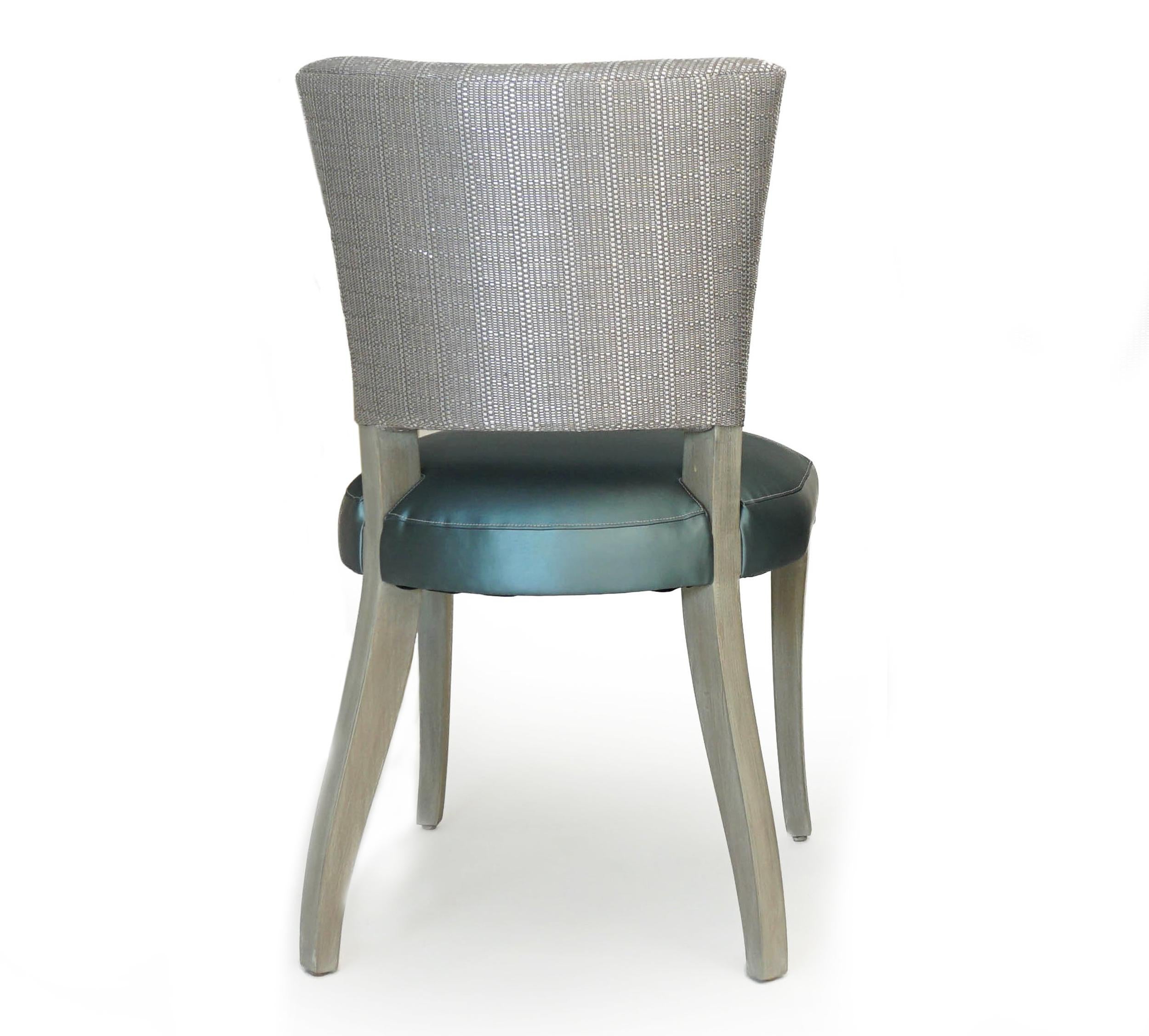 Transitional open back dining chair upholstered in blue and gold vinyl fabric with metallic woven back. This dining chair frame is solid hard maple featuring a Swedish finish. The sturdy saber legs and armless design make for easy dining. This chair