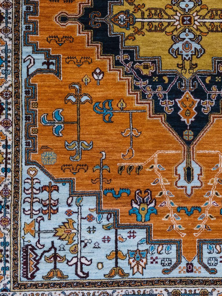 Dans des tons vifs d'orange, de bleu et de crème, ce tapis en pure laine, tissé selon une méthode persane traditionnelle, mesure environ 1,5 m x 1,5 m. Issu du renouveau tribal Orley Shabahang, ce motif inspiré du Serapi attire l'attention. Le champ