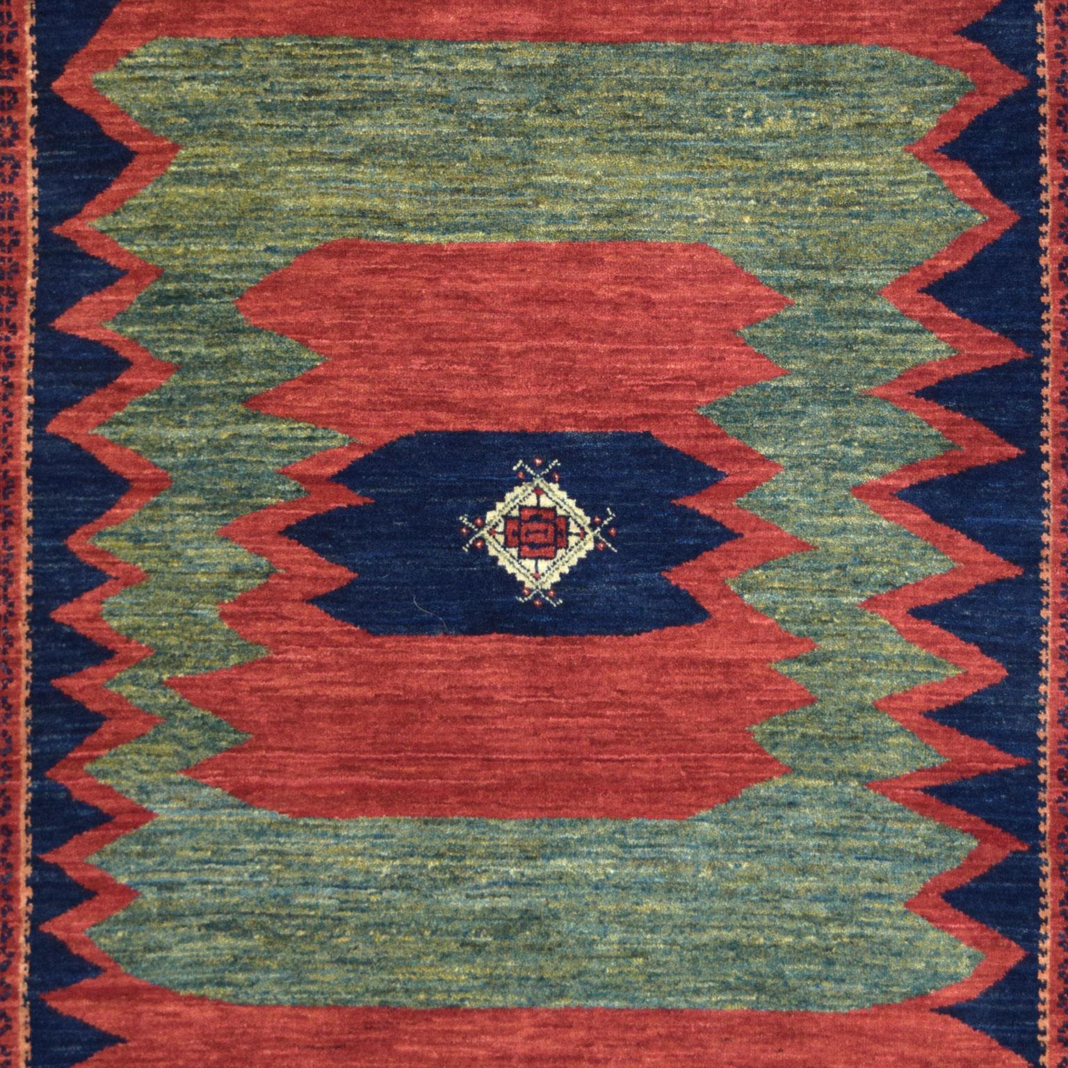 Pulling tribal inspirations from Persian Qashqai carpets, this hand-knotted rug, woven in rich green, red, indigo, and cream wool, measures 4’1”x 5’10” and belongs to the Orley Shabahang Tribal Collection. With a jagged and rudimentary interior