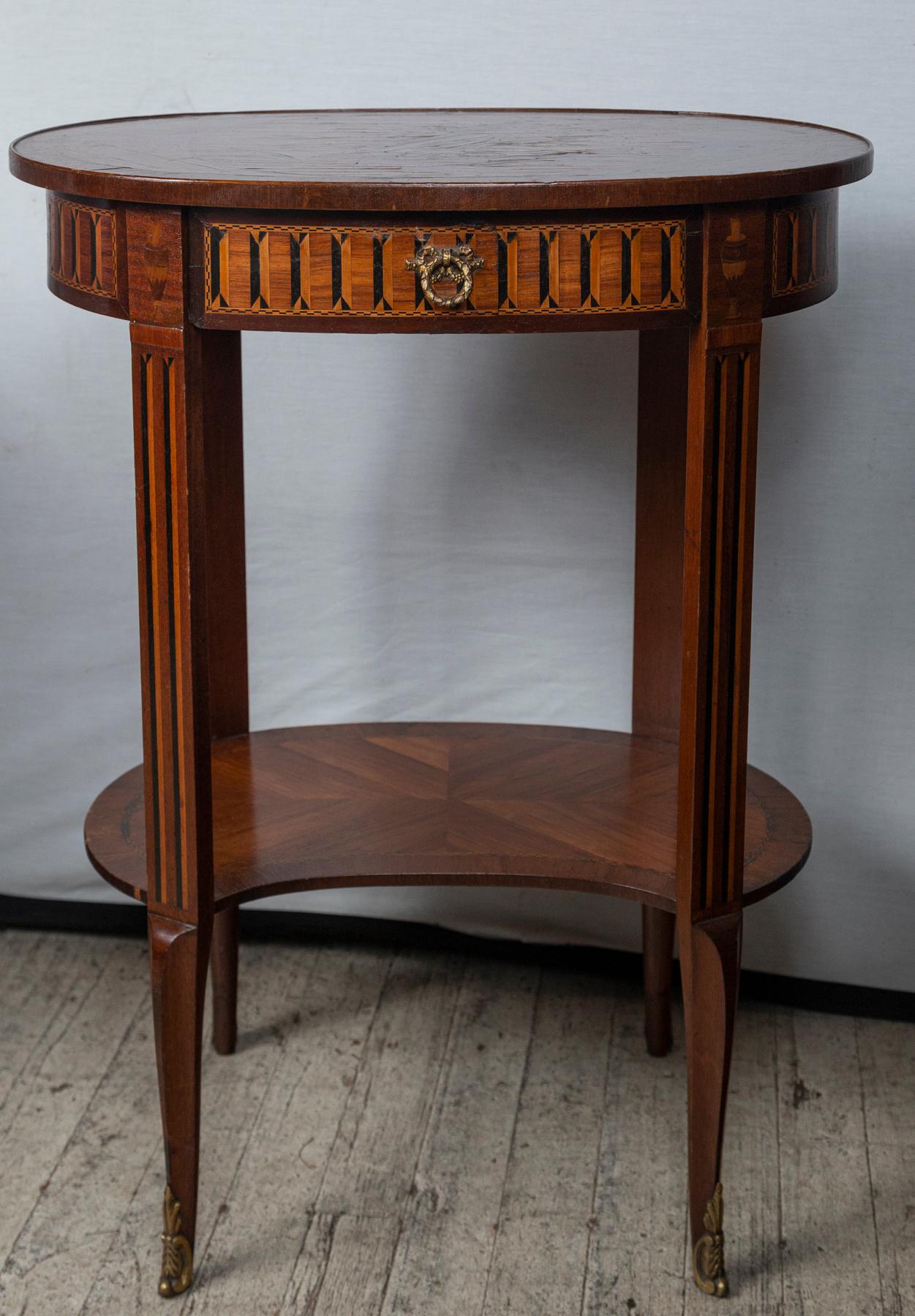 The oval table with transitional Louis XV/XVI legs ending it brass or bronze applied mounts, The lower shaped shelf of mahogany parquetry . The top designed with the same parquetry, surrounding a marquetry center panel , The marquetry of various