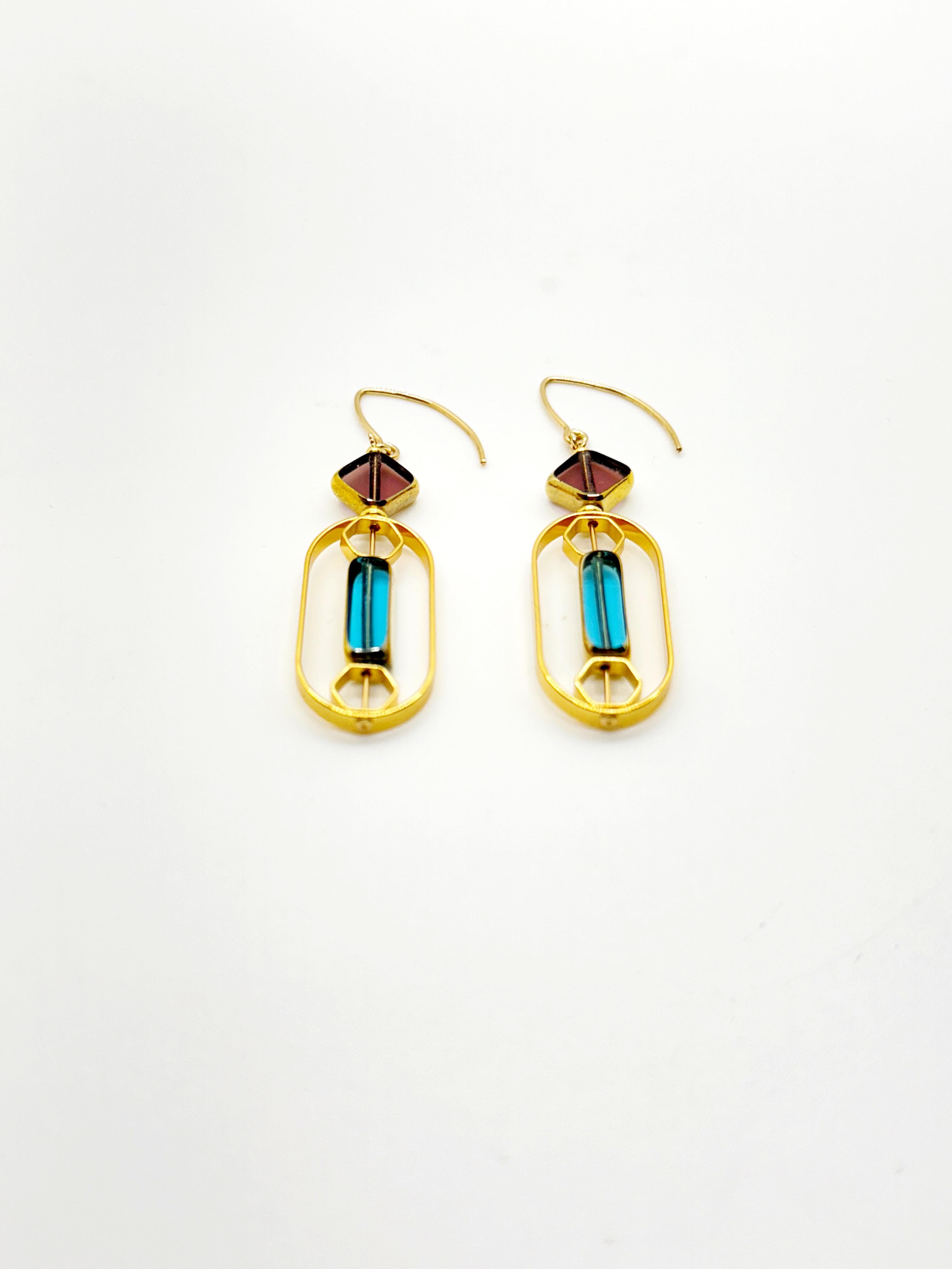 The earrings are lightweight and are made to rotate and reposition with movement.

The earrings consist of translucent burgundy and light blue new old stock vintage German glass beads that are framed with 24K gold. The beads were hand-pressed during
