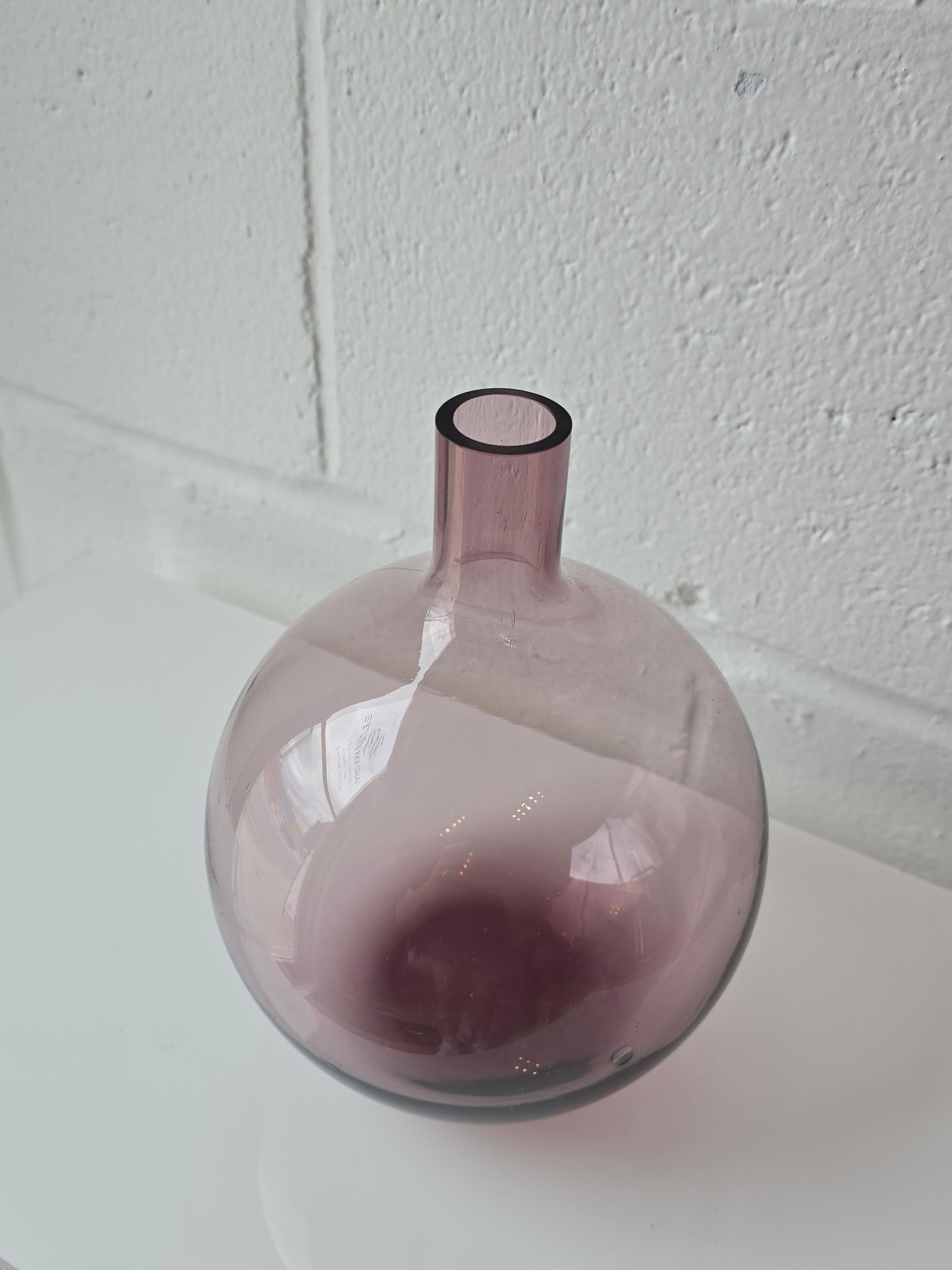 Verre d'art transparent de couleur violet améthyste dans un vase en forme de bulbe. Ce récipient est fabriqué à partir d'un verre d'art transparent à pigments violets, de forme arrondie et à l'embouchure étroite, rappelant la forme d'un bulbe. Il