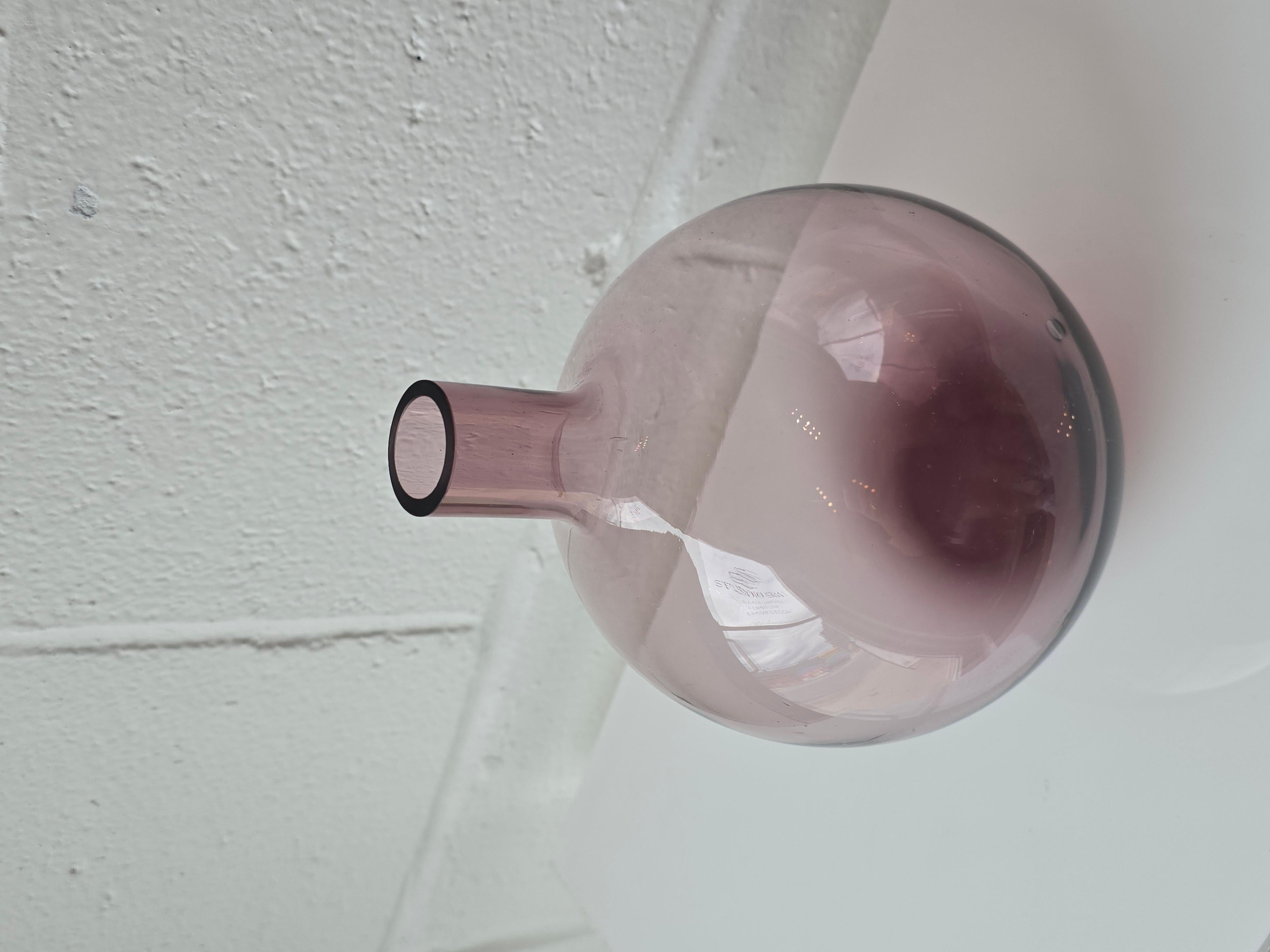 Verre d'art transparent de couleur violet améthyste dans un vase en forme de bulbe. Ce récipient est fabriqué à partir d'un verre d'art transparent à pigments violets, de forme arrondie et à l'embouchure étroite, rappelant la forme d'un bulbe. Il