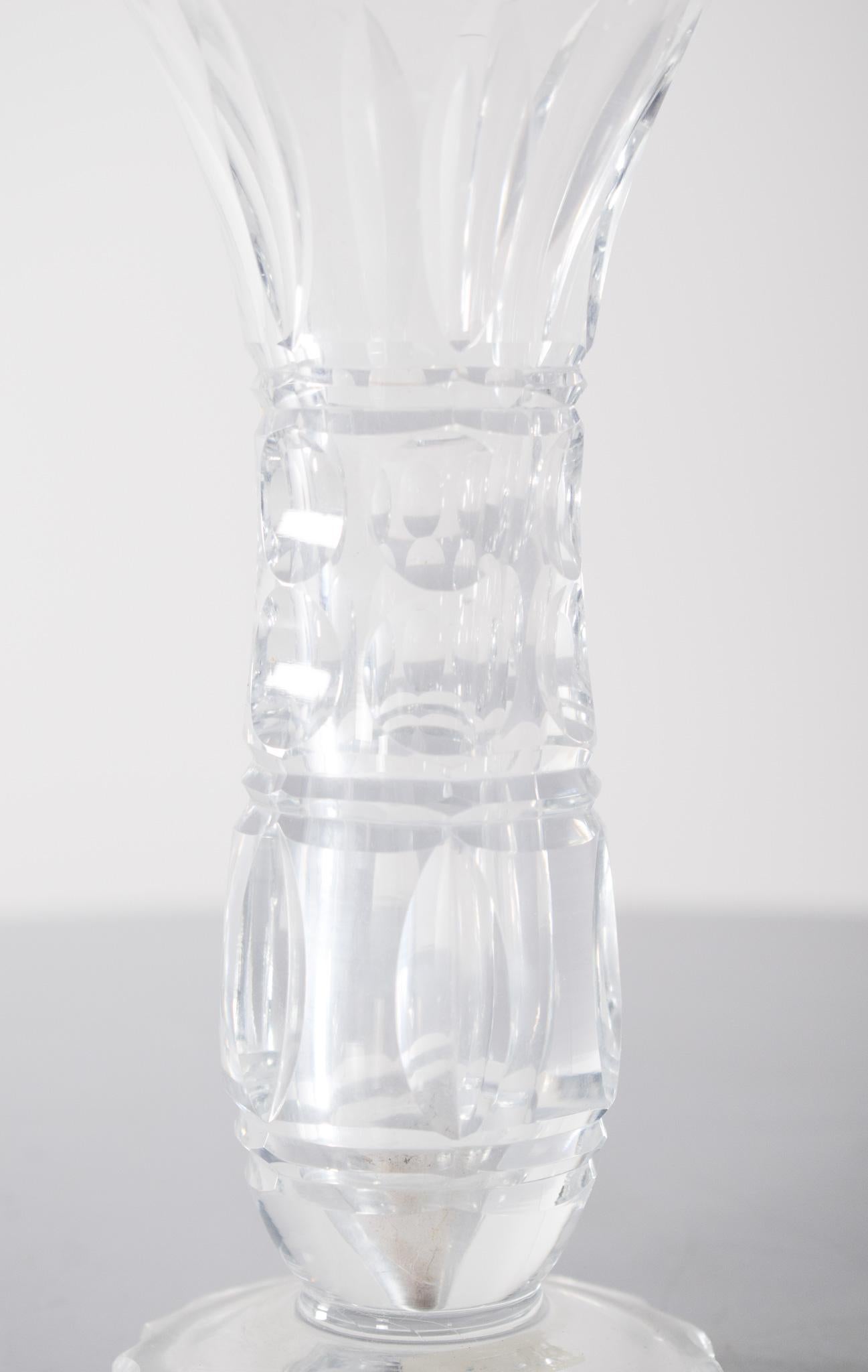 Clear glass vase. With a slender body, the glass is faceted and highlights the reflection of light. With a thick circular base decorated with beveled cuts, the stem is delicately carved, with oval motifs in relief that give it texture. The bulge