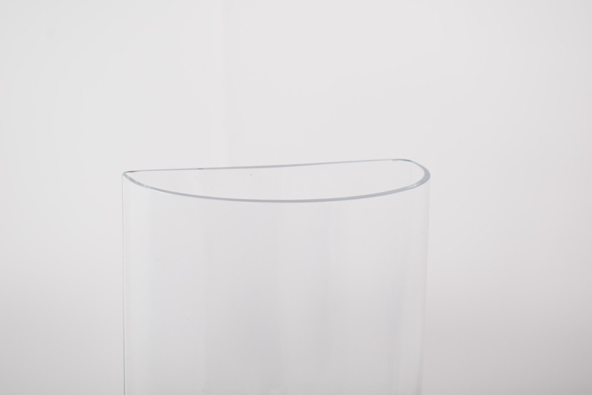Vaso in vetro trasparente a forma di mezzaluna. Con un design contemporaneo e forme geometriche morbide, la sua struttura è composta da un mezzo cilindro con base arrotondata e vertici leggermente allungati, creando un profilo di originalità ed