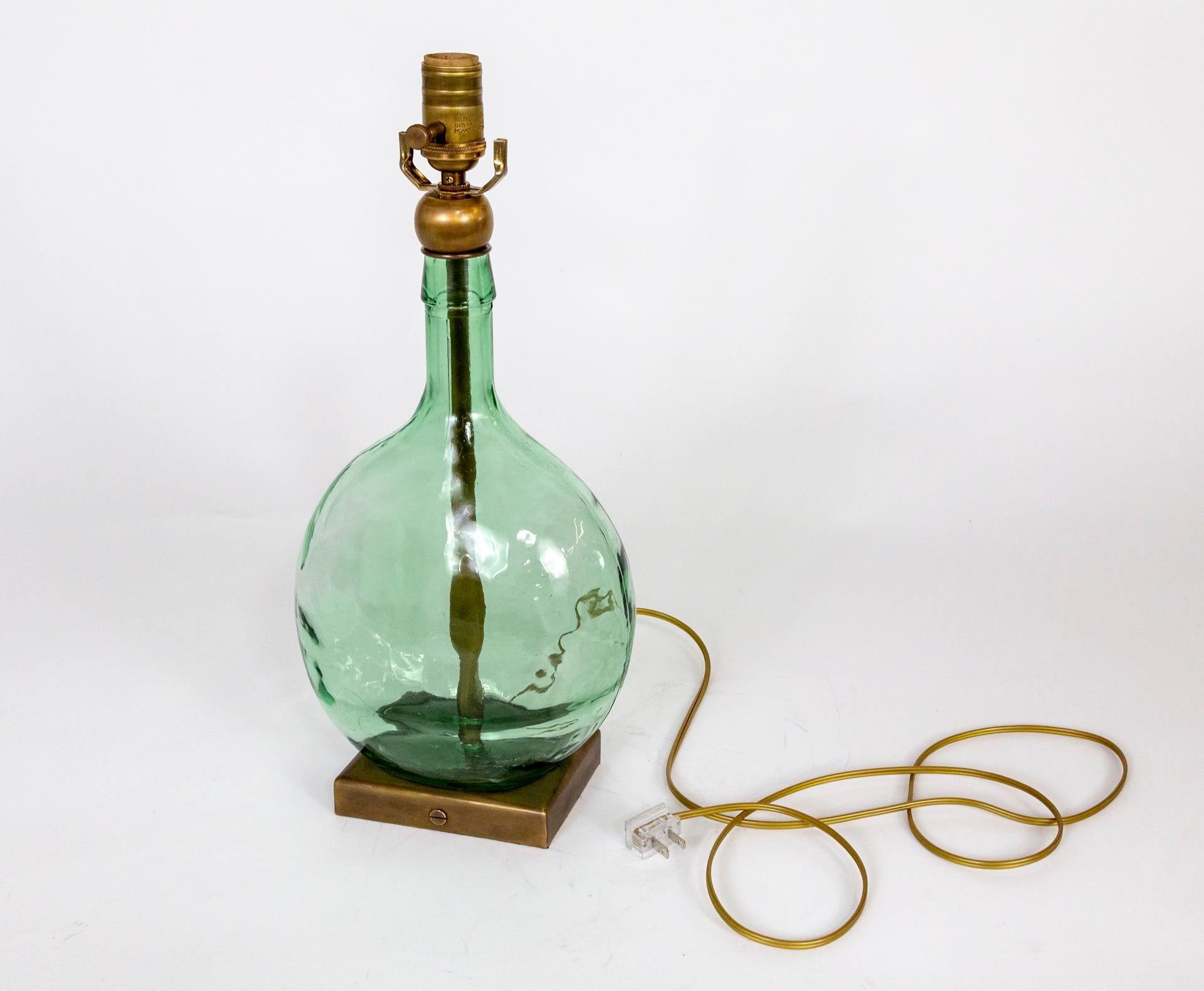 This is a large, translucent green, gourd-shaped bottle with a rippled effect on glass fashioned as a sleek lamp. It has slim depth and is mounted on a rectangular, brass base and capped with a brass ball. Newly wired with a dimmer on the socket.