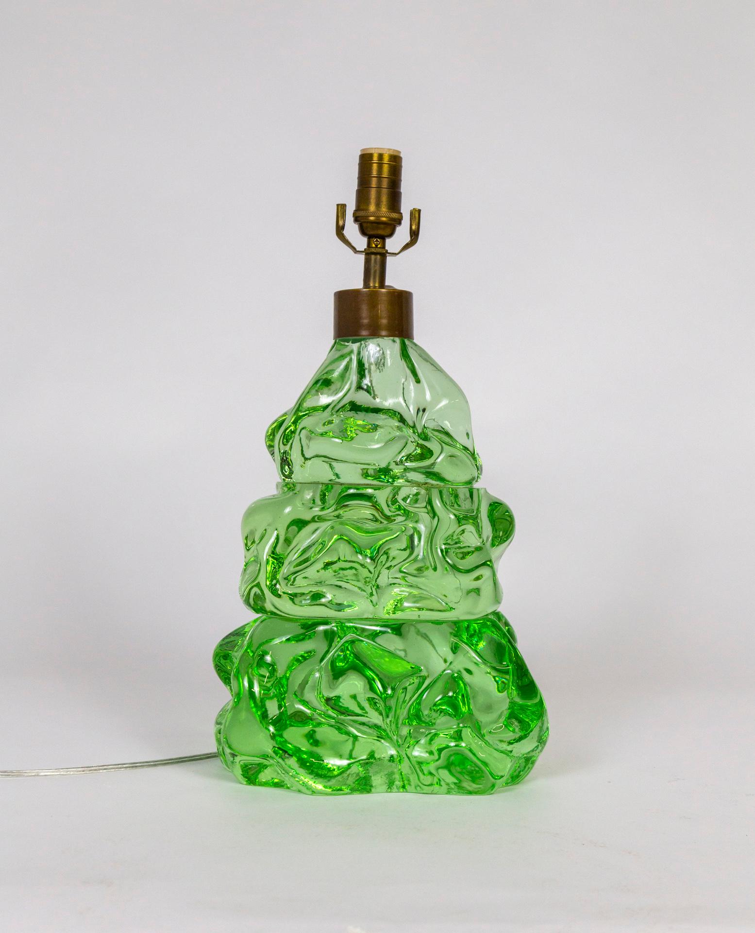 A whimsical, bulbous, tree form in heavy, green glass is French wired as a lamp. It takes on different looks depending on what is behind it and on what ground it sits; shifting color and value. It's comprised of three stacked pieces. With new brass