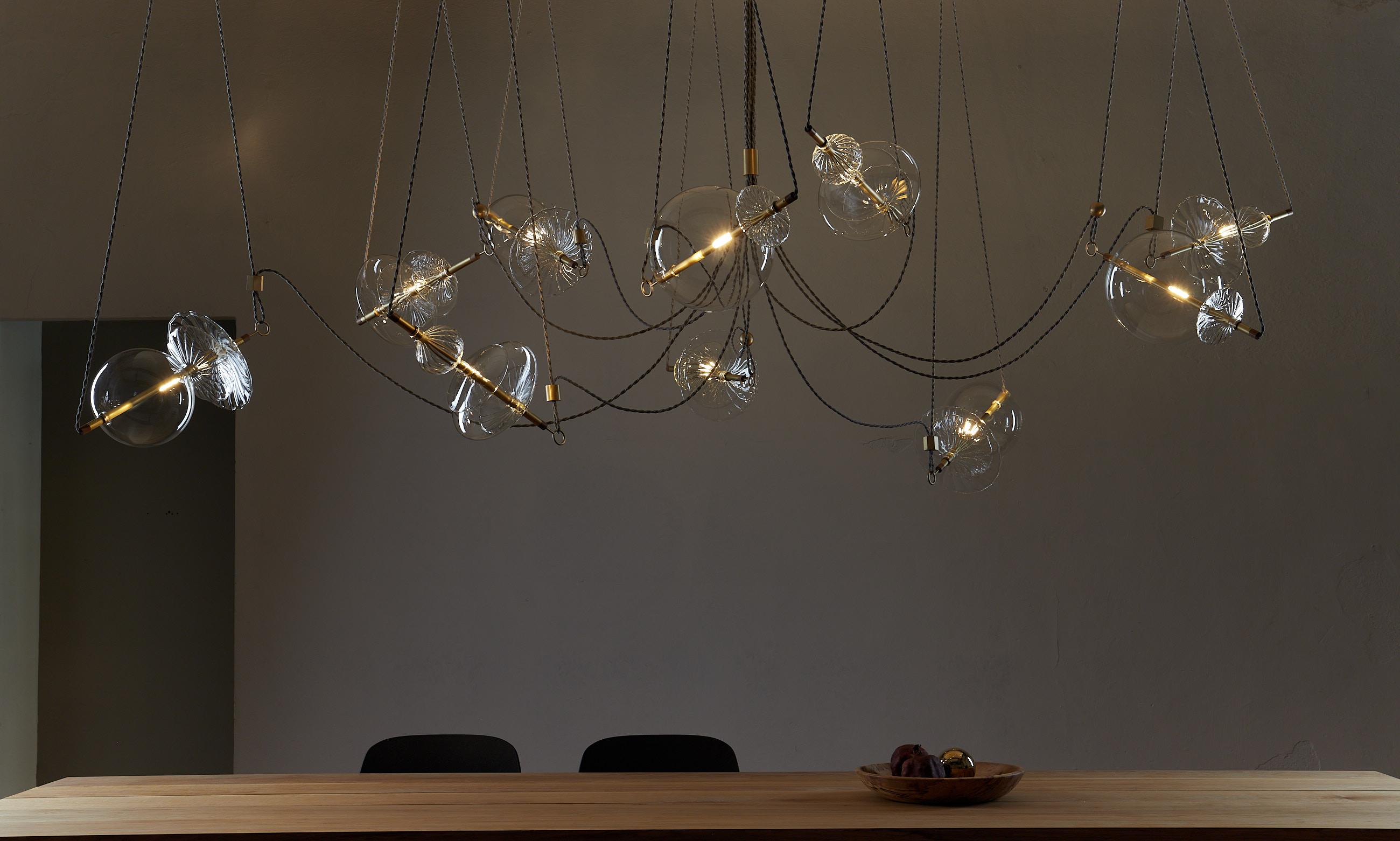 The Trapezi contemporary chandelier is inspired by the idea of a Circus Trapeze Artist.

Hand blown glass in a variety of forms and colors is combined with brass bars and hung by Linen Cords from hub units on the ceiling.
The glass is left