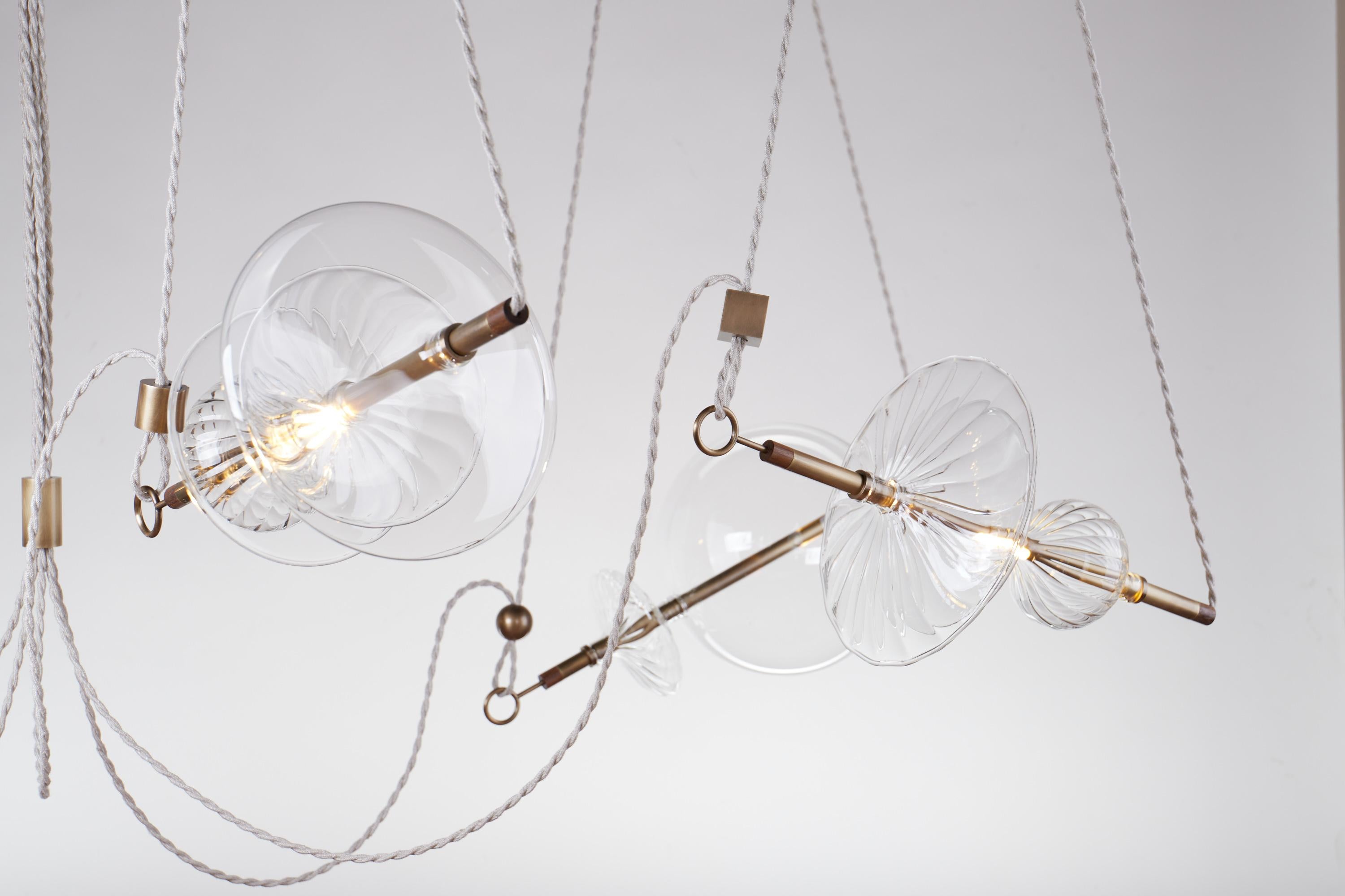 The Trapezi contemporary chandelier is inspired by the idea of a Circus Trapeze artist.

Hand-blown glass in a variety of forms is combined with brass bars and hung by Linen Cords from hub units on the ceiling.

The arrangement of the lights is