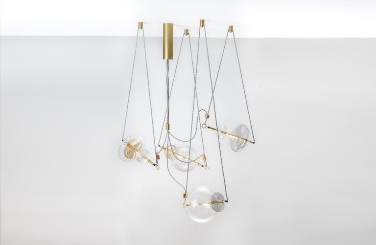 The Trapezi contemporary chandelier is inspired by the idea of a Circus Trapeze Artist.

Hand-blown glass in a variety of forms and colors is combined with brass bars and hung by Linen Cords from hub units on the ceiling.
The glass is transparent