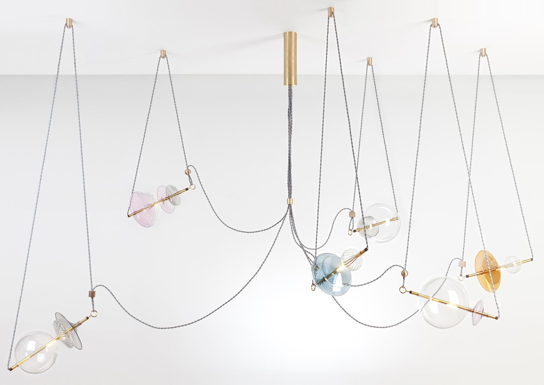 The Trapezi contemporary chandelier is inspired by the idea of a Circus Trapeze Artist.

Hand blown glass in a variety of forms and colors is combined with brass bars and hung by Linen Cords from hub units on the ceiling.
The glass is left