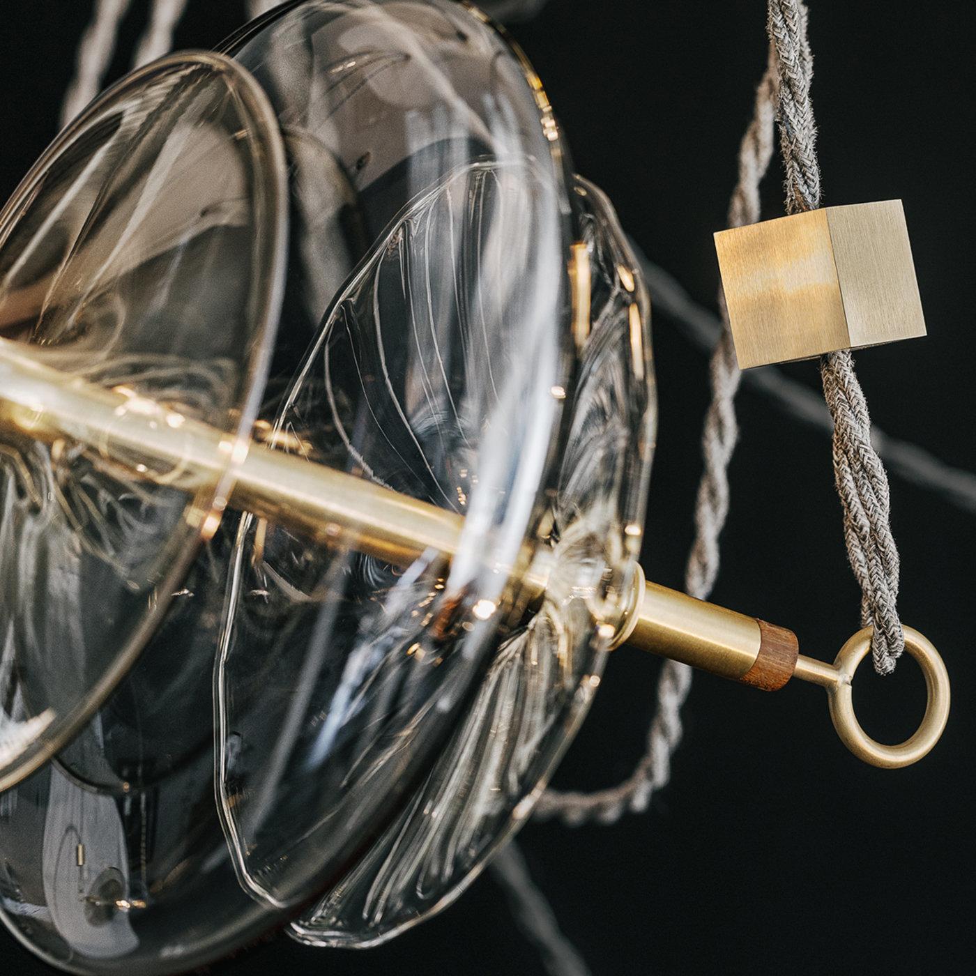 This contemporary chandelier is inspired by a circus trapeze and its form allows for the lights to be adjusted separately in any direction. The glass elements are hand blown in different forms linked by brass bars and hung on linen cords from hub