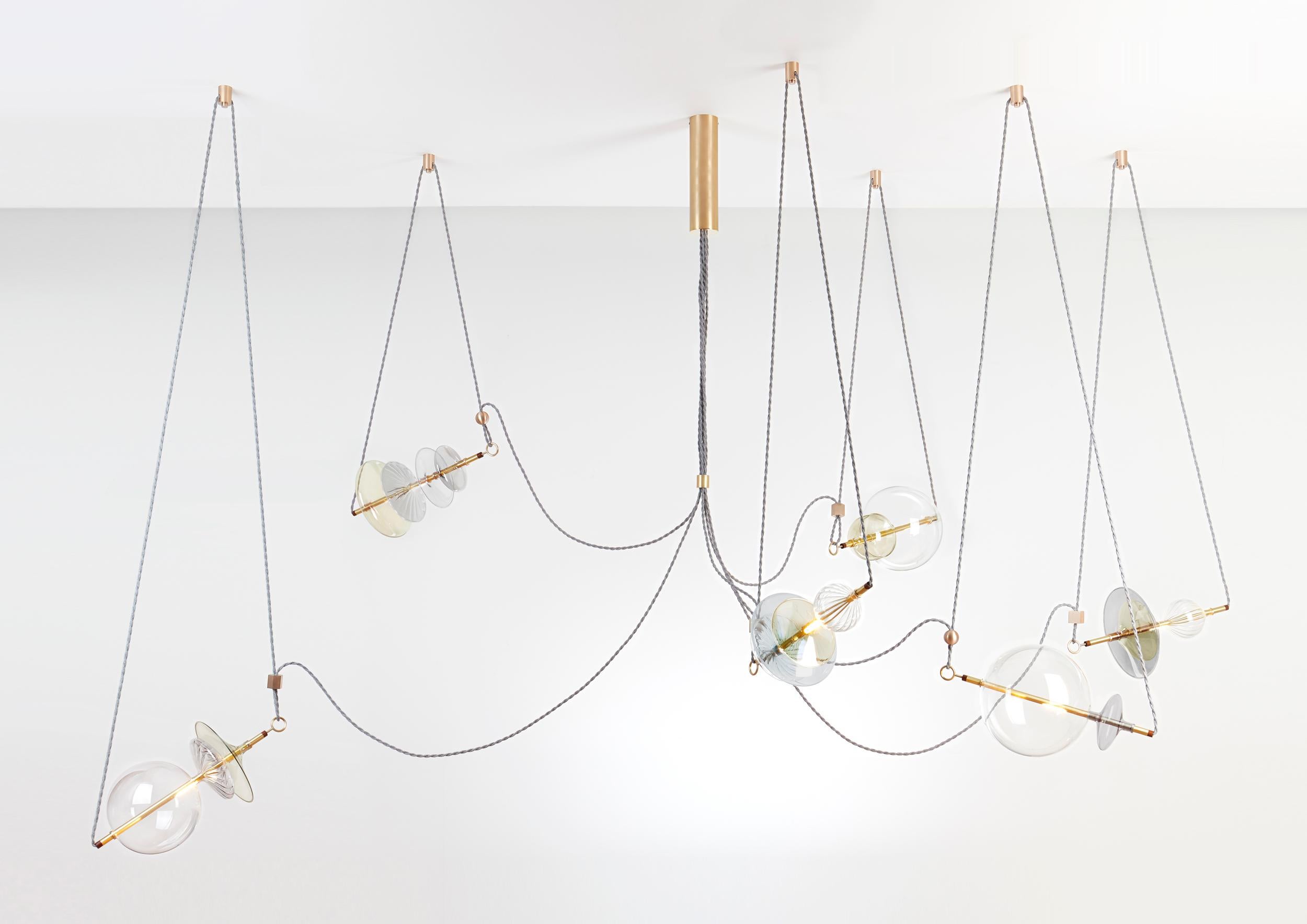 The Trapezi contemporary chandelier is inspired by the idea of a Circus Trapeze Artist.

Hand blown glass in a variety of forms and colors is combined with brass bars and hung by Linen Cords from hub units on the ceiling.
The glass is left