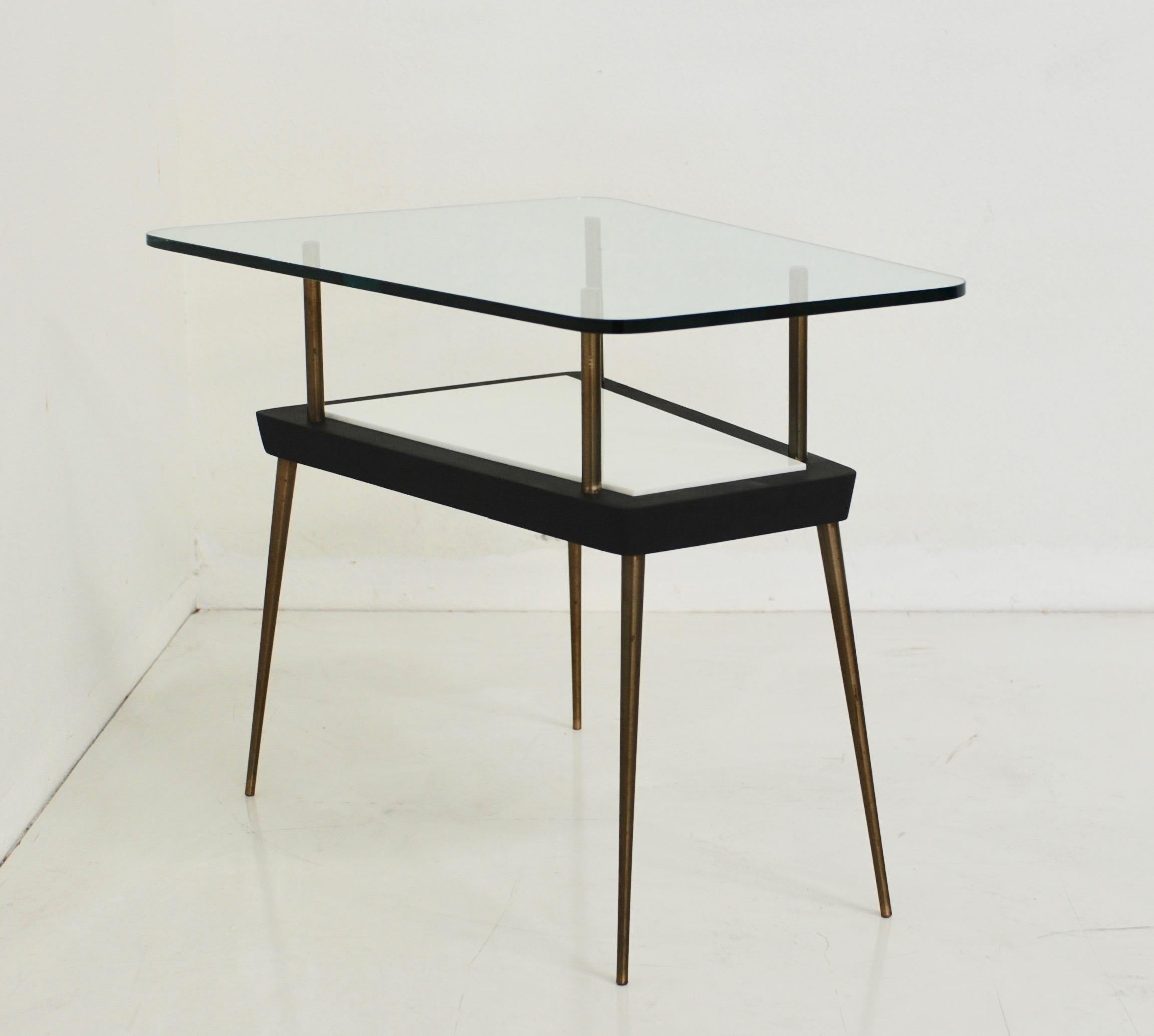 An Italian or French side or end table is made of wood with a white glass insert and clear glass top and elegant thin brass legs. The trapezoid shape of the table is softened with rounded edges. A beautiful elegant example of midcentury style.