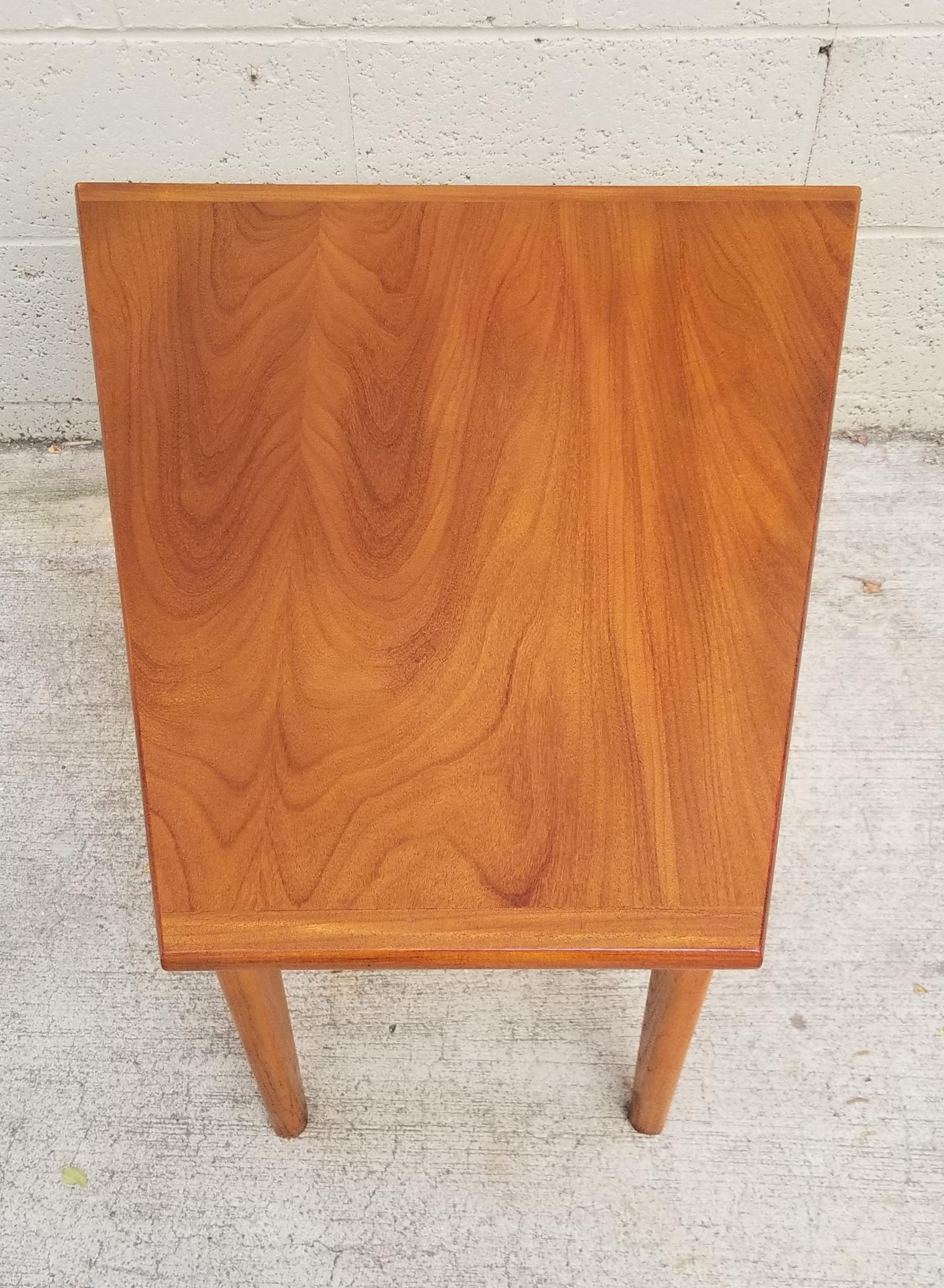 A Mid-Century Modern trapezoid end table with bold, finger-joint construction. Quality materials and workmanship. Notice exceptional wood grain to top surface. Excellent vintage condition with original finish. 

Front width measures 11.88 inches.