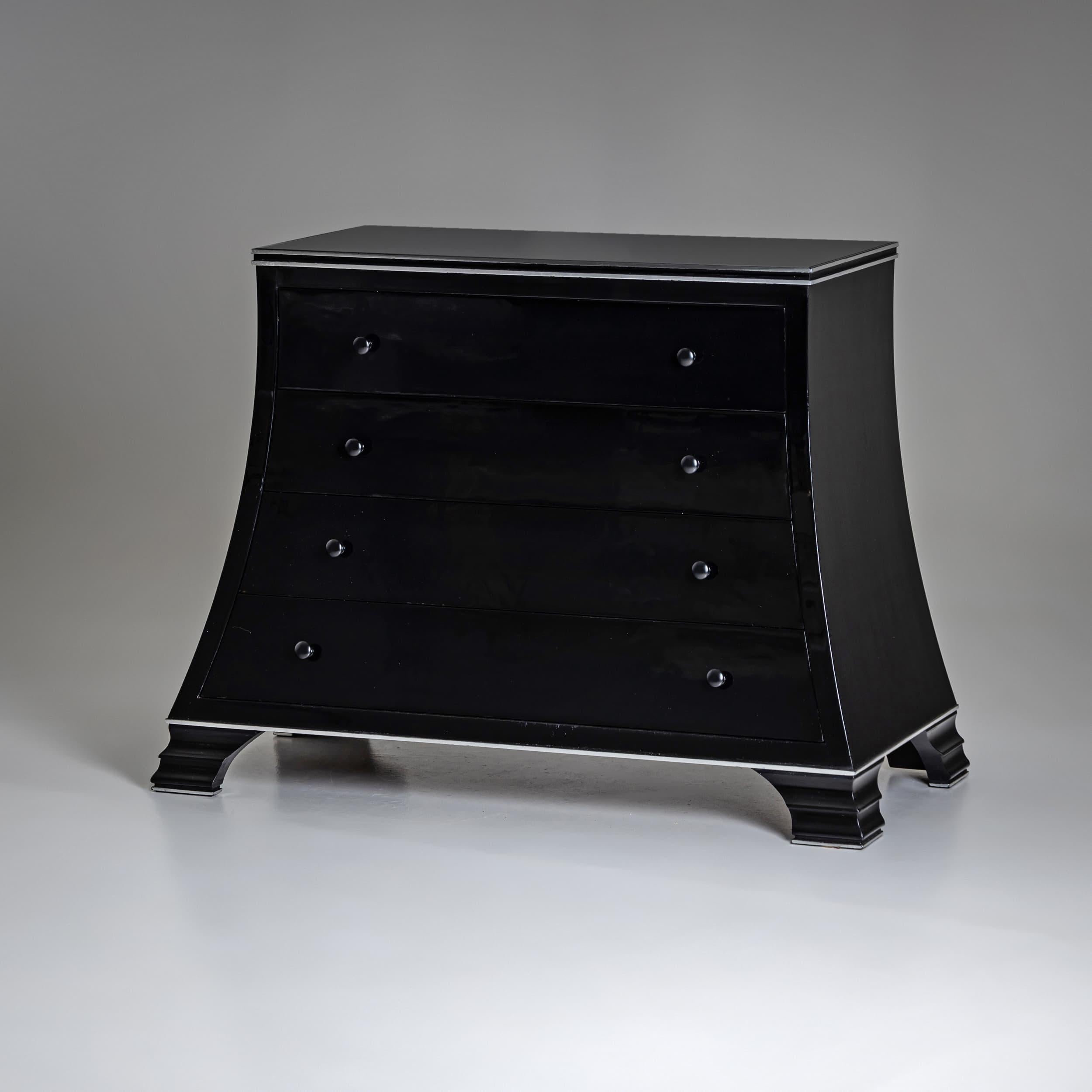 Moderna toilette nera con quattro cassetti e un corpo trapezoidale che poggia su gambe a gradini. I manici sono in metallo, mentre i bordi sono argentati per completare il design, dando al pezzo un aspetto elegante e senza tempo.