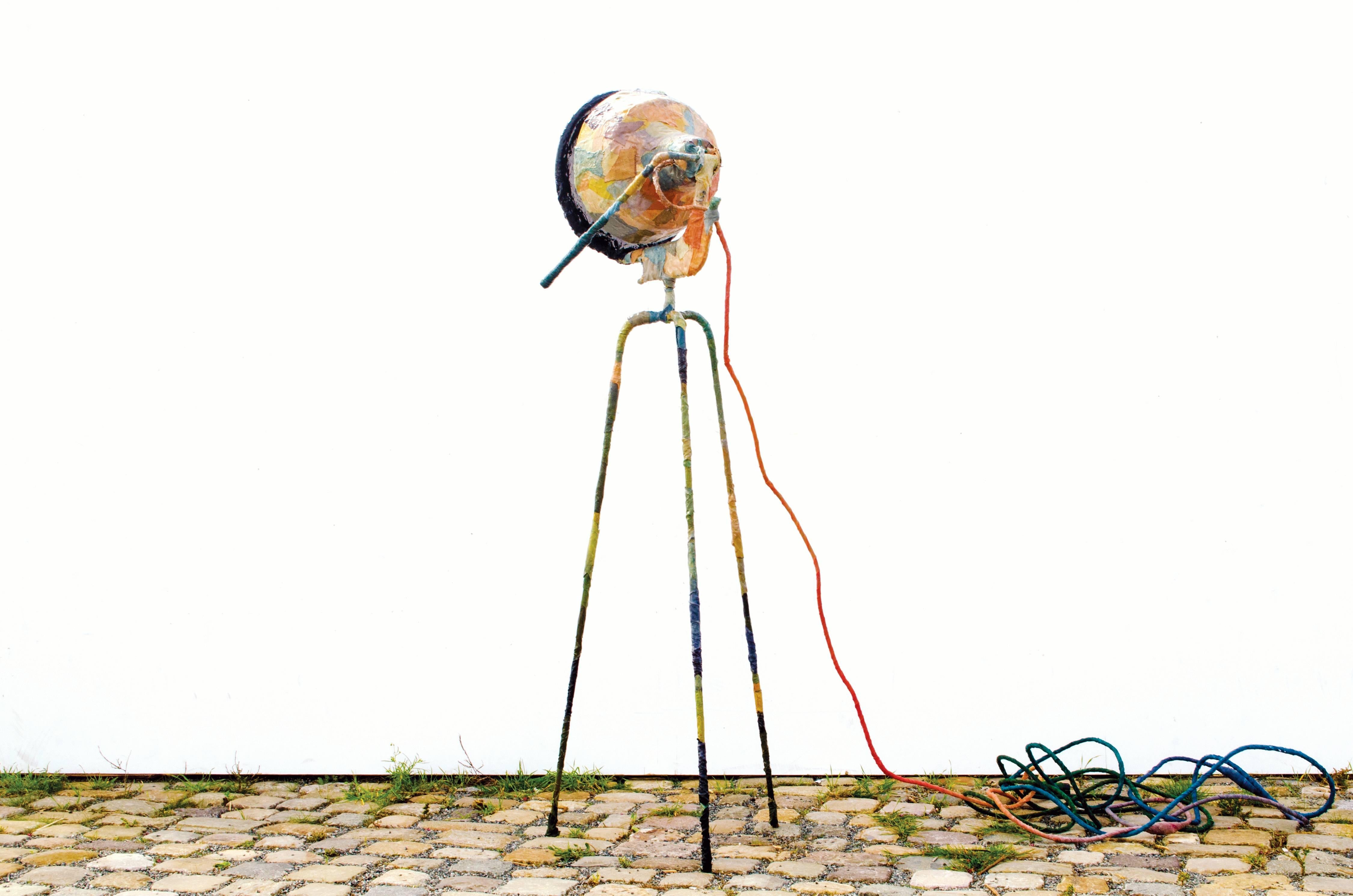 This three-legged floor lamp is covered in fabric waste that merged into a new skin.
The lamp has a fine blend of colors and a rough appearance.
The lamp is fully adjustable
A black screen dims the light.