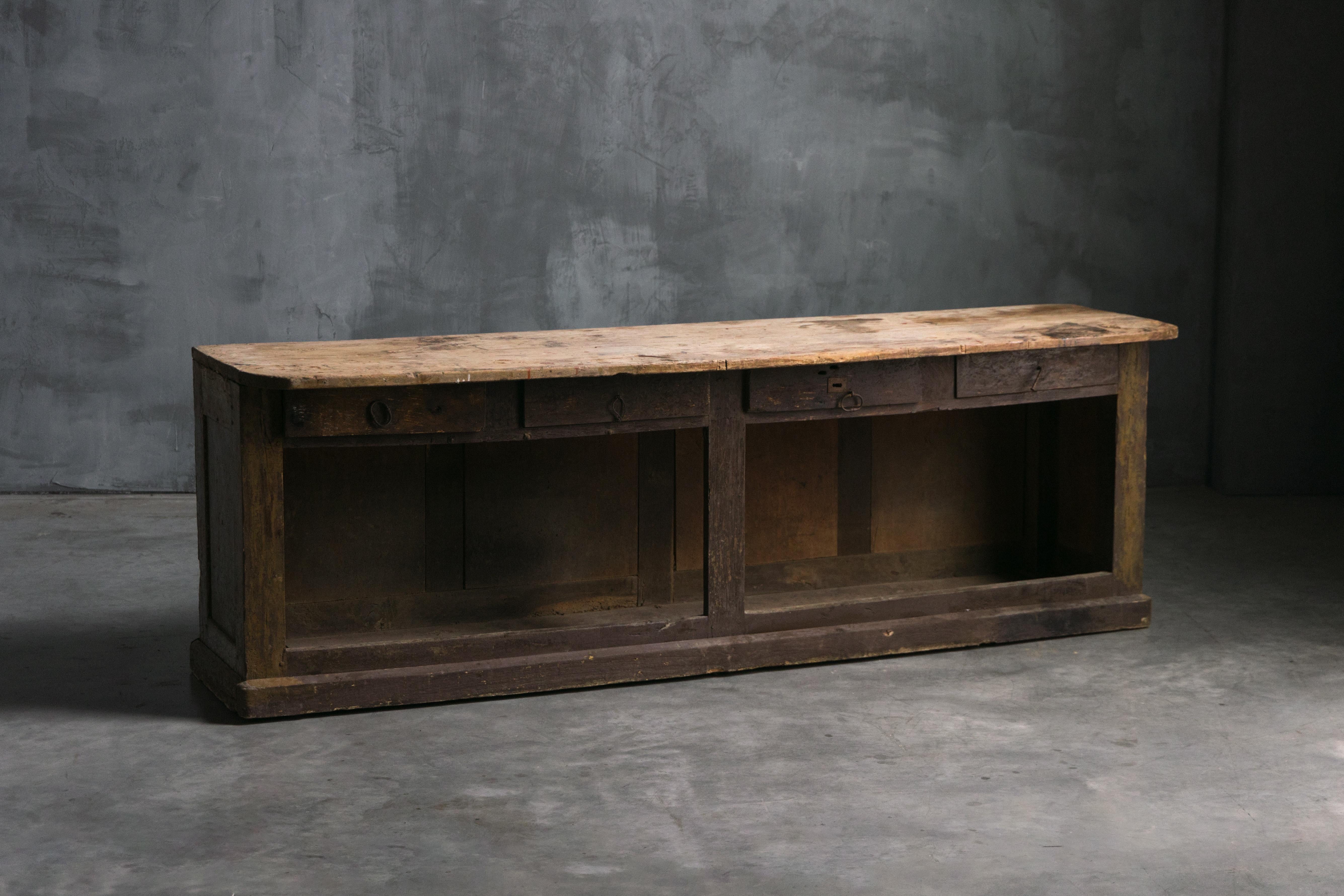 19th-century French shop counter that combines rustic charm with practical functionality. Featuring closed front panels, open storage at the back, and four convenient drawers, it can serve as a freestanding counter, workbench, or bar in any creative