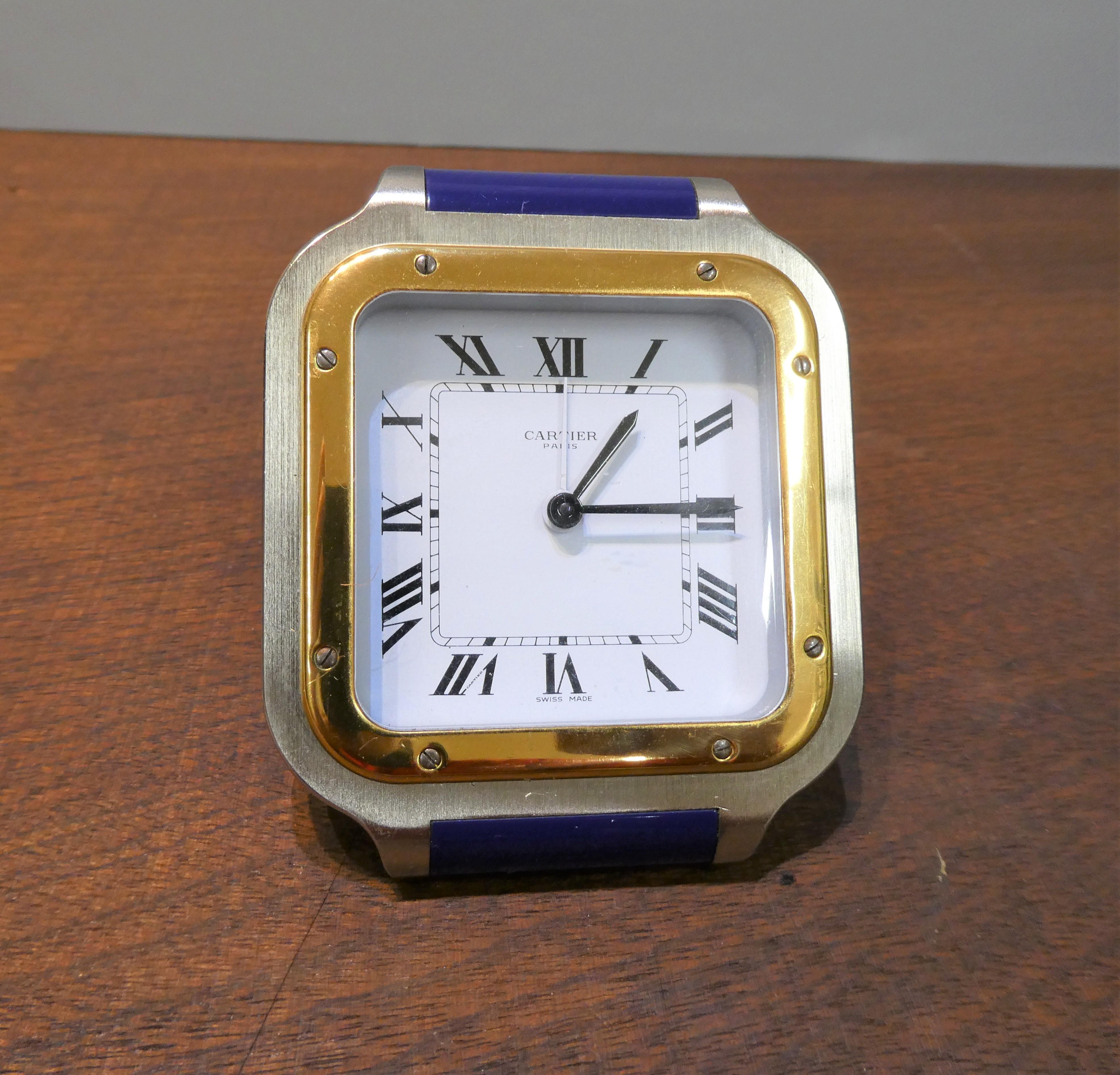 Cartier Reiseuhr

Rechteckiger Strebenrahmen aus gebürstetem Stahl mit Lapis Lazuli-Einsätzen. 
Die Messinglünette umrahmt ein gemaltes Zifferblatt mit römischen Ziffern, Originalzeigern und Weckerzeiger, signiert 'Cartier'.

Vergoldeter