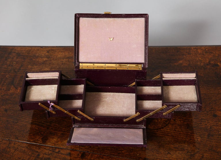 A very attractive burgundy leather woman's traveler's jewel box with original key. Expands on hinges for display. Lower full tray, two divided mid trays, and two top trays with ring holder slots. English, early 20th century.