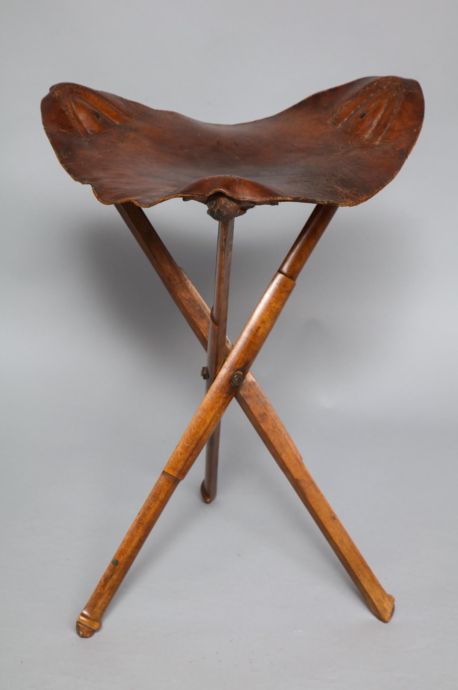 A stylish traveling stool with original leather seat on mahogany tripod frame folding to a stick with brass center pin. Used originally for picnicking or campaigning, now not strong enough for seating but good as a clothes-horse in a bedroom or
