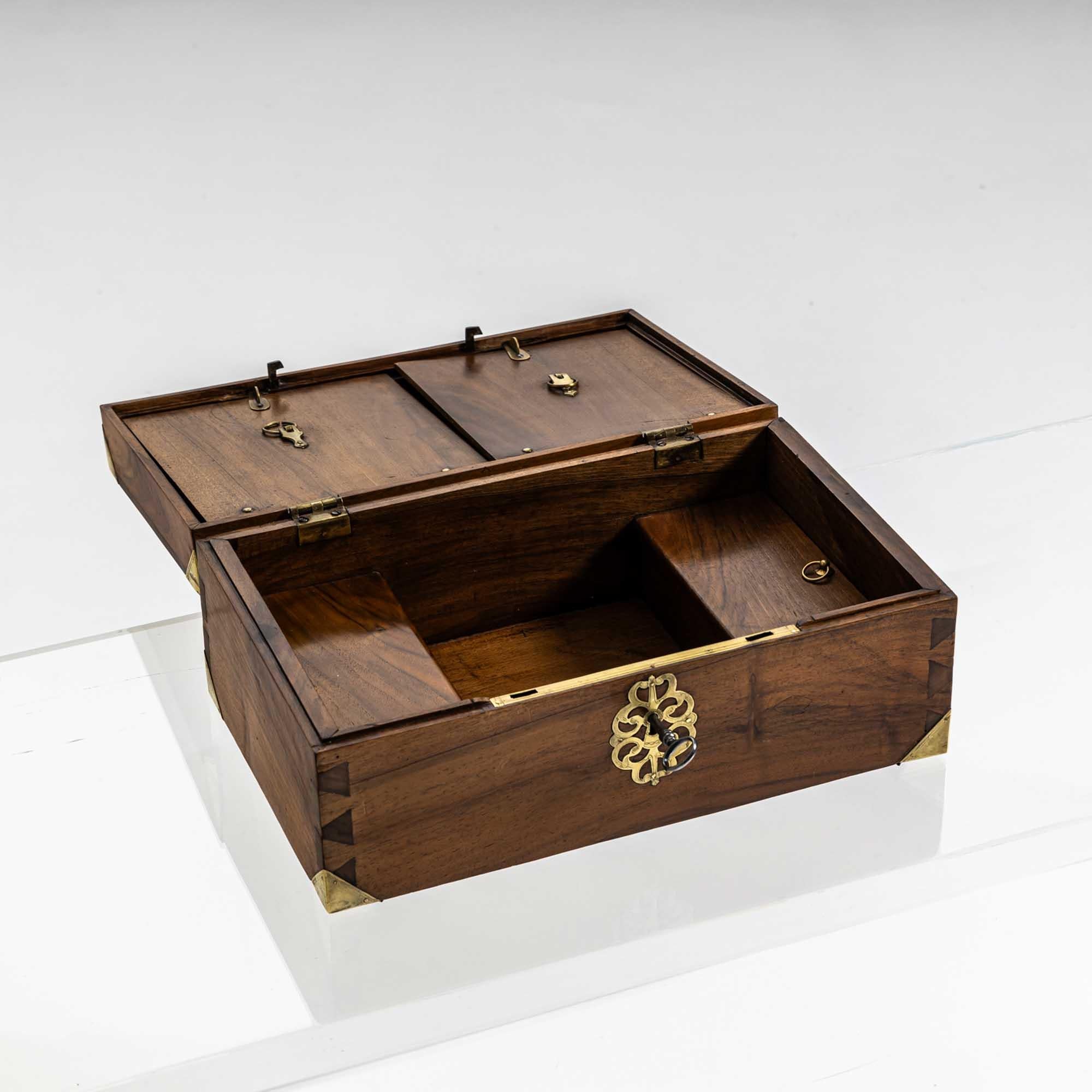 Cassapanca rettangolare in legno di noce con finiture in ottone agli angoli e una maniglia sul coperchio. L'interno è diviso in scomparti più piccoli e in lembi che possono essere fissati con piccoli ganci. 