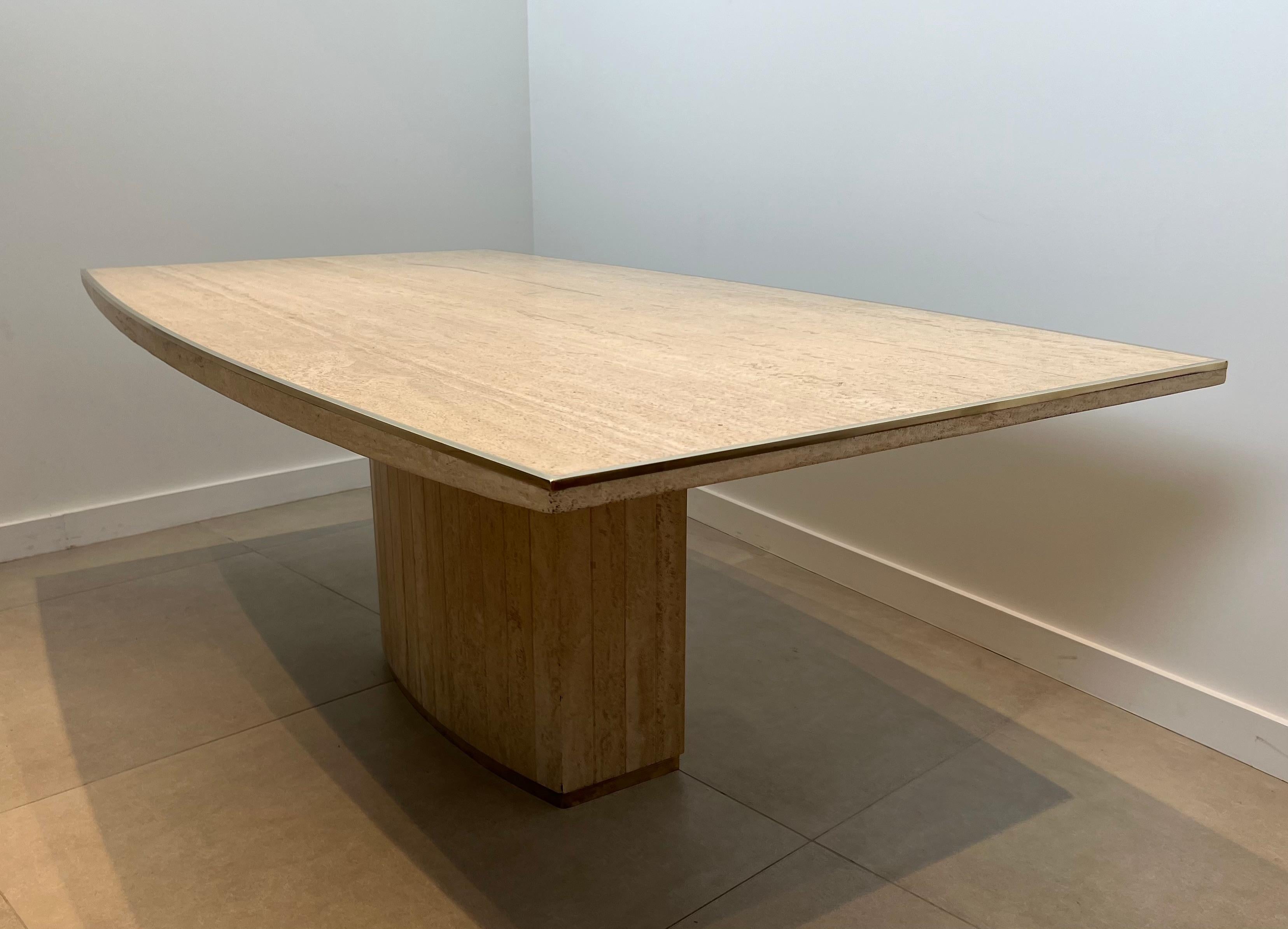 Cette magnifique et très élégante table de salle à manger en forme de tonneau est composée d'un très beau plateau en travertin avec un filet de laiton sur les côtés du plateau ainsi que sur la base. Il s'agit d'une œuvre du célèbre designer Willy