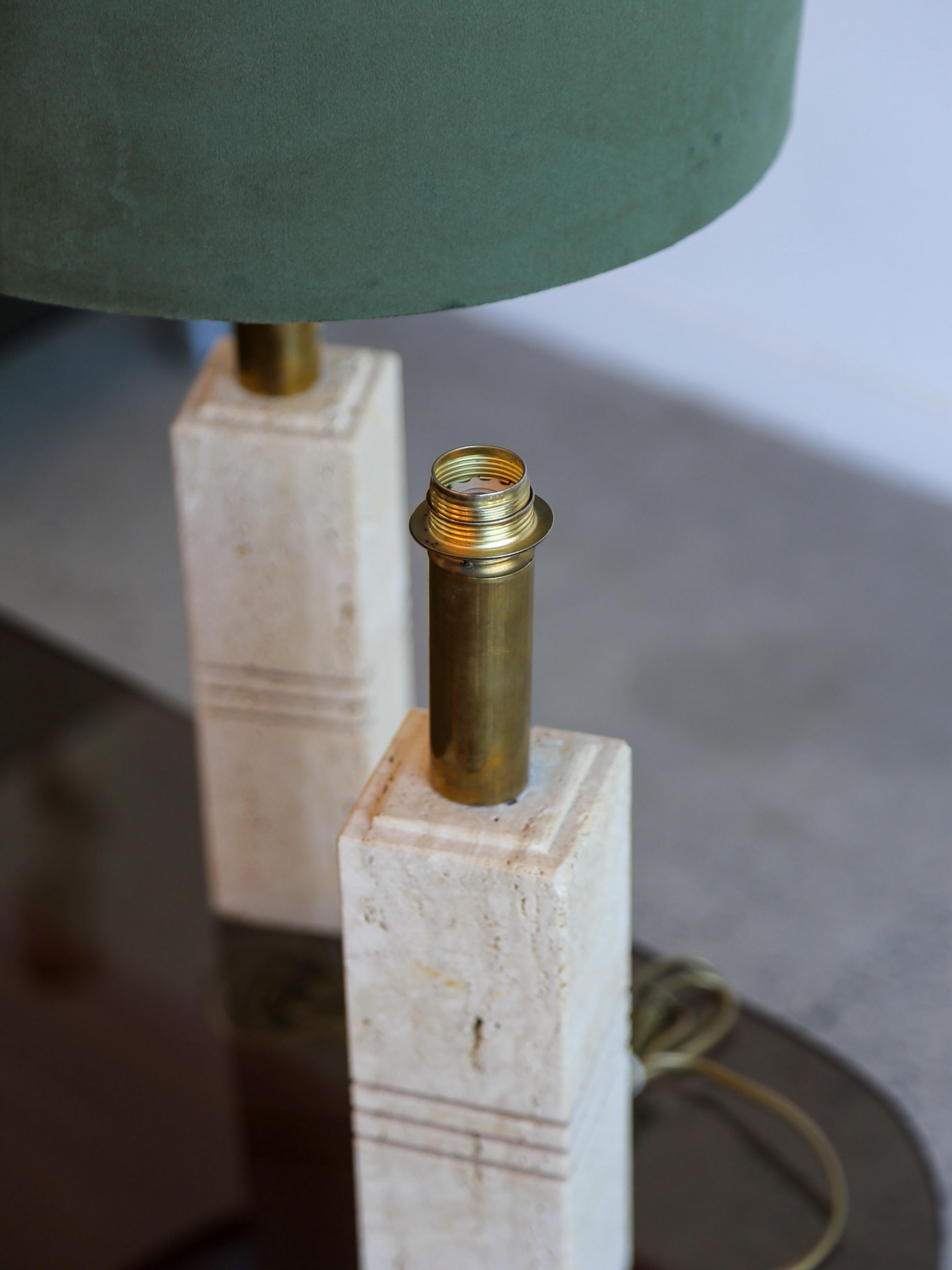 Featuring a deep green velvet drum shade, a warm brass-finished stem, and a distinctive travertine stone base etched with subtle linear accents, this lamp brings both texture and elegance to any space. Perfect for bedside tables, living rooms, or
