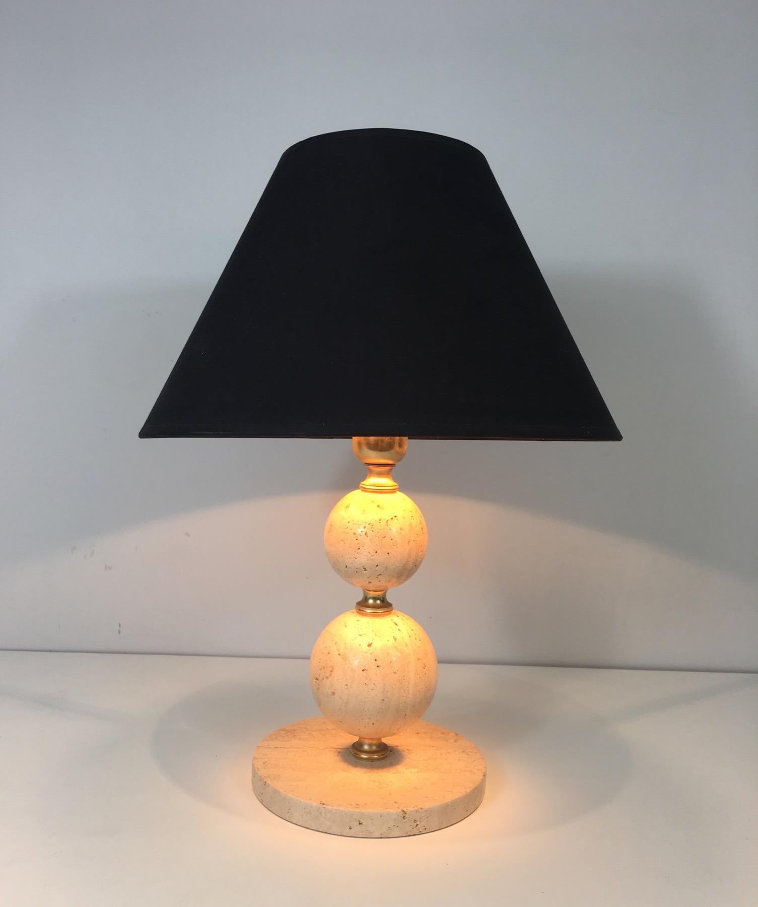 This table lamp is made of travertine with an interesting design composed of two travertine spheres separated by brass pieces. The custom shade is made of a black shintz gilt inside. This is a French work, circa 1970.