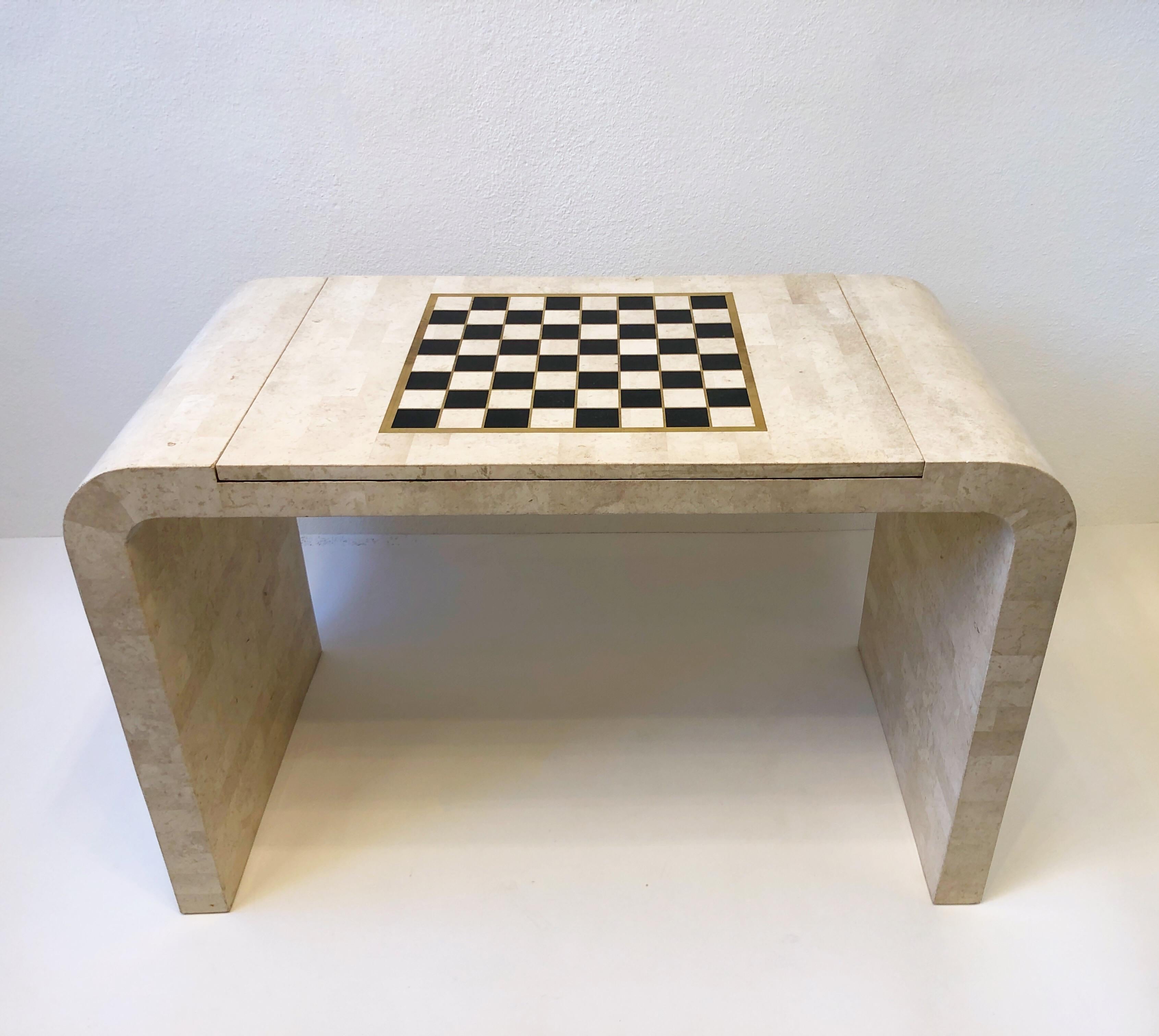 Glamorous 1980’s tessellated travertine and marble with brass inlaid waterfall game table by Maitland Smith. 
The table is constructed of wood with tessellated travertine covering it the Brass outlines the game boards. The back gammon pieces are