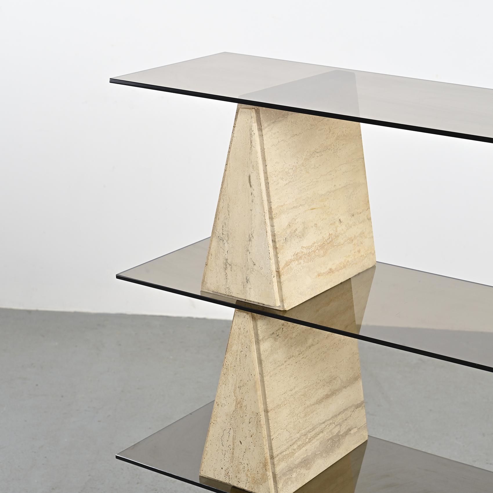 
Bookshelf composed of six triangular travertine blocks, supporting rectangular shelves in smoked black glass.

We appreciate the elegant contrast between the raw, natural travertine and the transparency of the glass.

Italy, circa 1970.
