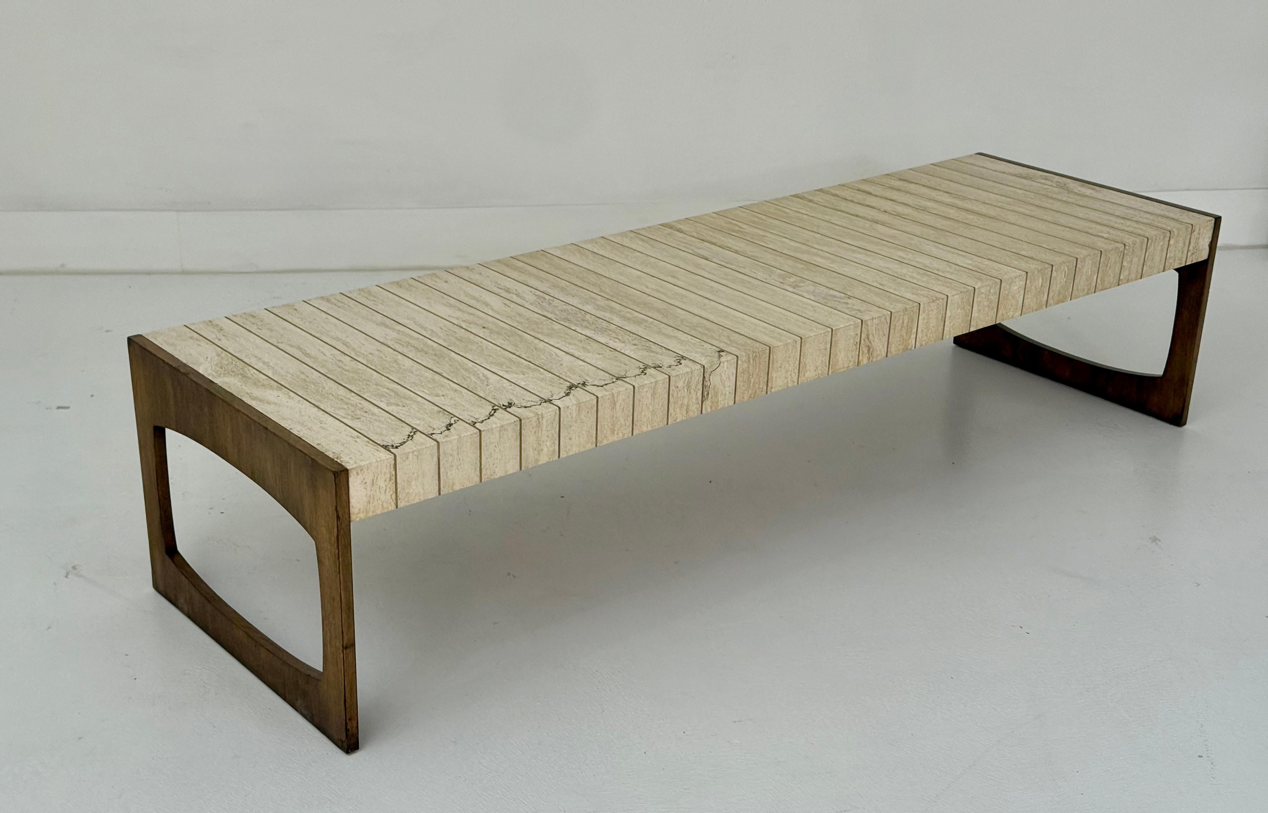A striking example of refined Mid-Century American design, this cocktail table by Baker Furniture dates to the 1950s and showcases a harmonious blend of travertine, walnut, and brass. The top is composed of sculptural travertine slabs arranged in a