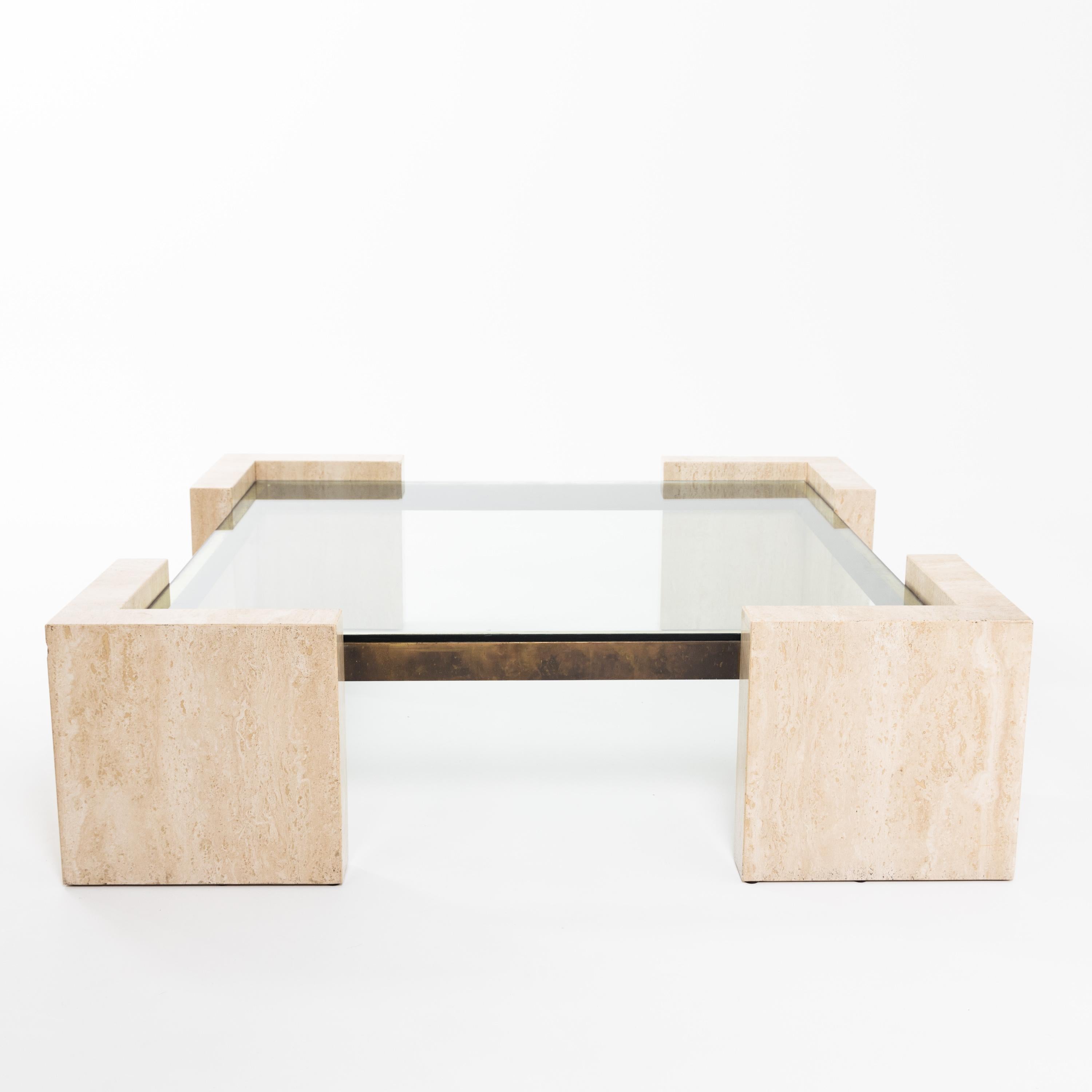 Large coffee table in square base form with brass frame, thick glass top and L-shaped supports in smooth, light beige travertine.
 