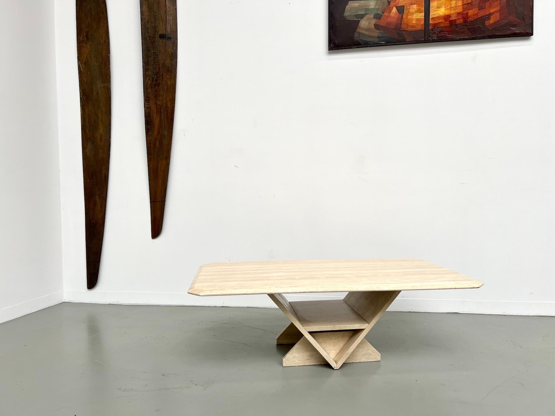 Maison Lecan presenta esta mesa de centro de travertino fabricada en Italia en los años 70.

La encimera rectangular con bordes achaflanados descansa sobre una base central de X cruzada, una composición geométrica a la vez sobria y escultórica. Este