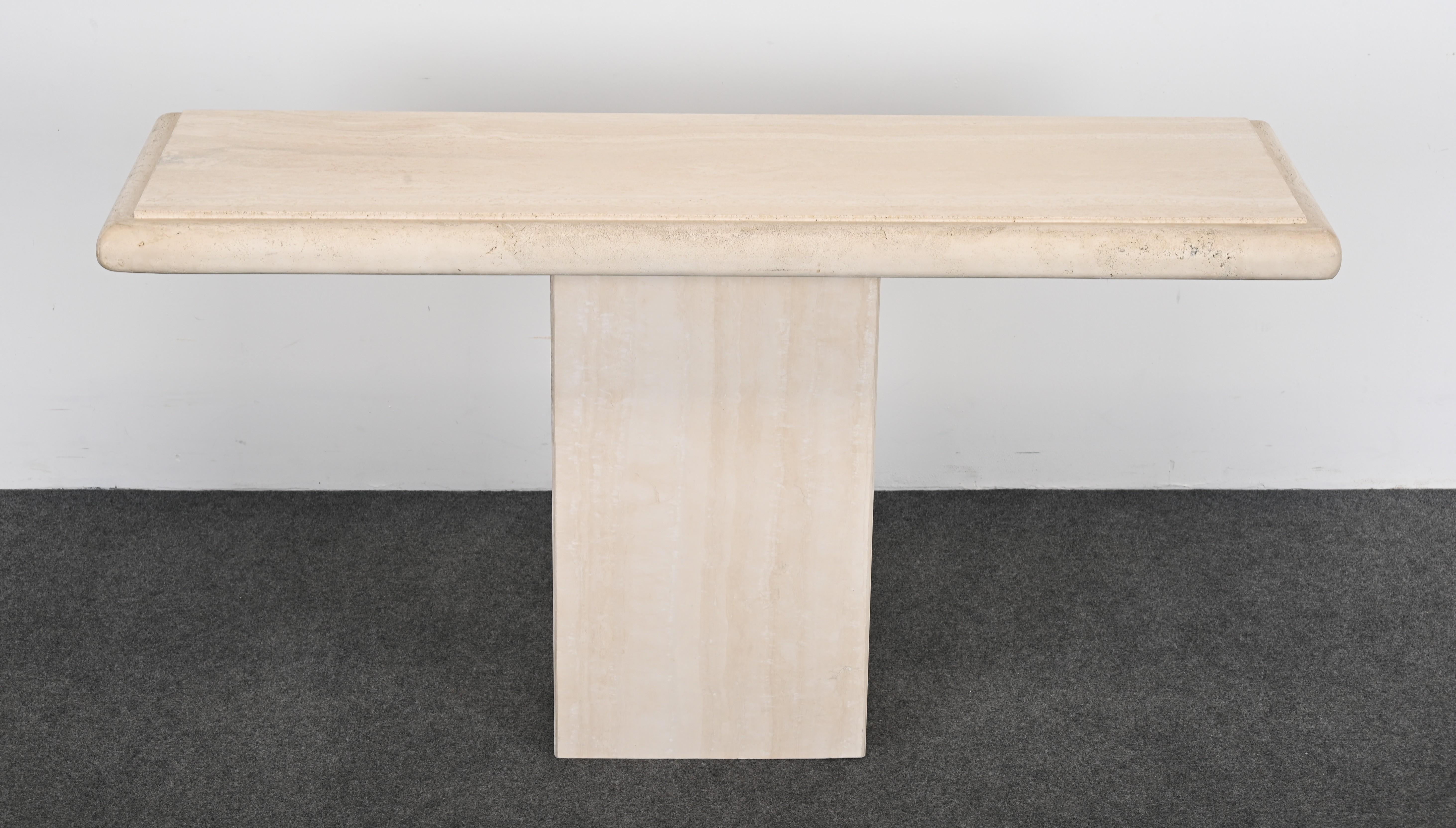 A minimalist beige Roche Bobois-style travertine marble console with natural beveled edges. This console table would look great in an entryway or accenting a beautiful sculpture as shown in the images. This pedestal table comes in two parts. It is
