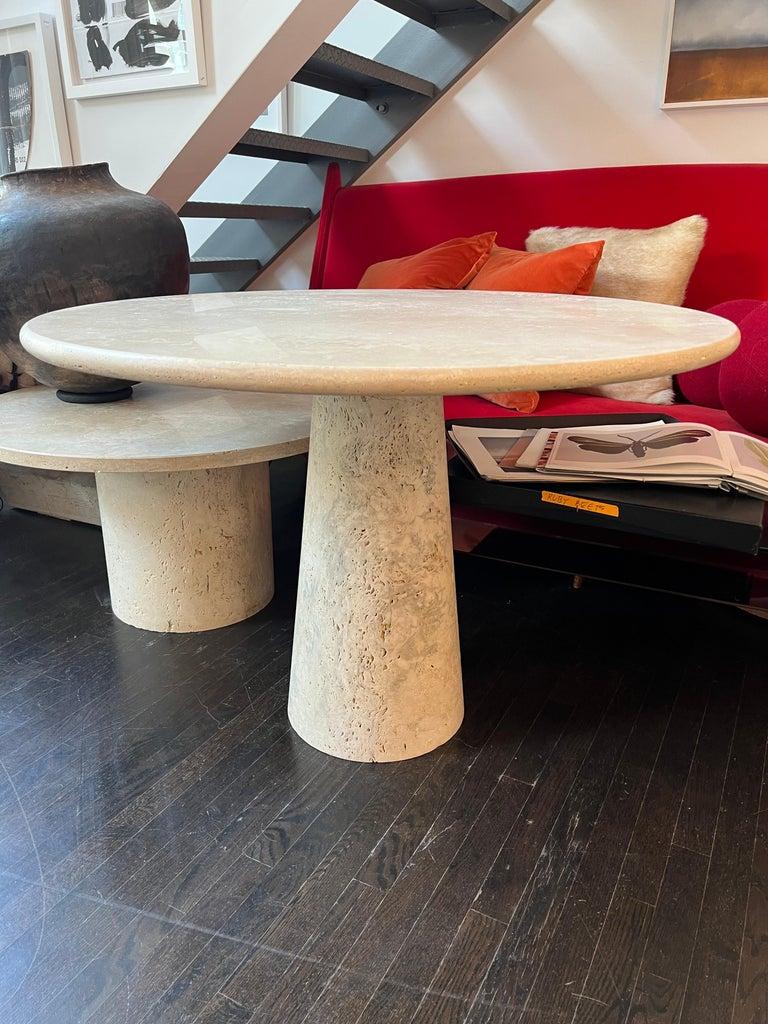 Table en travertin romain blanc par Le Lampade. 
Le plateau rond en travertin est soutenu par une base conique en travertin. Ces tables peuvent être fabriquées sur mesure.