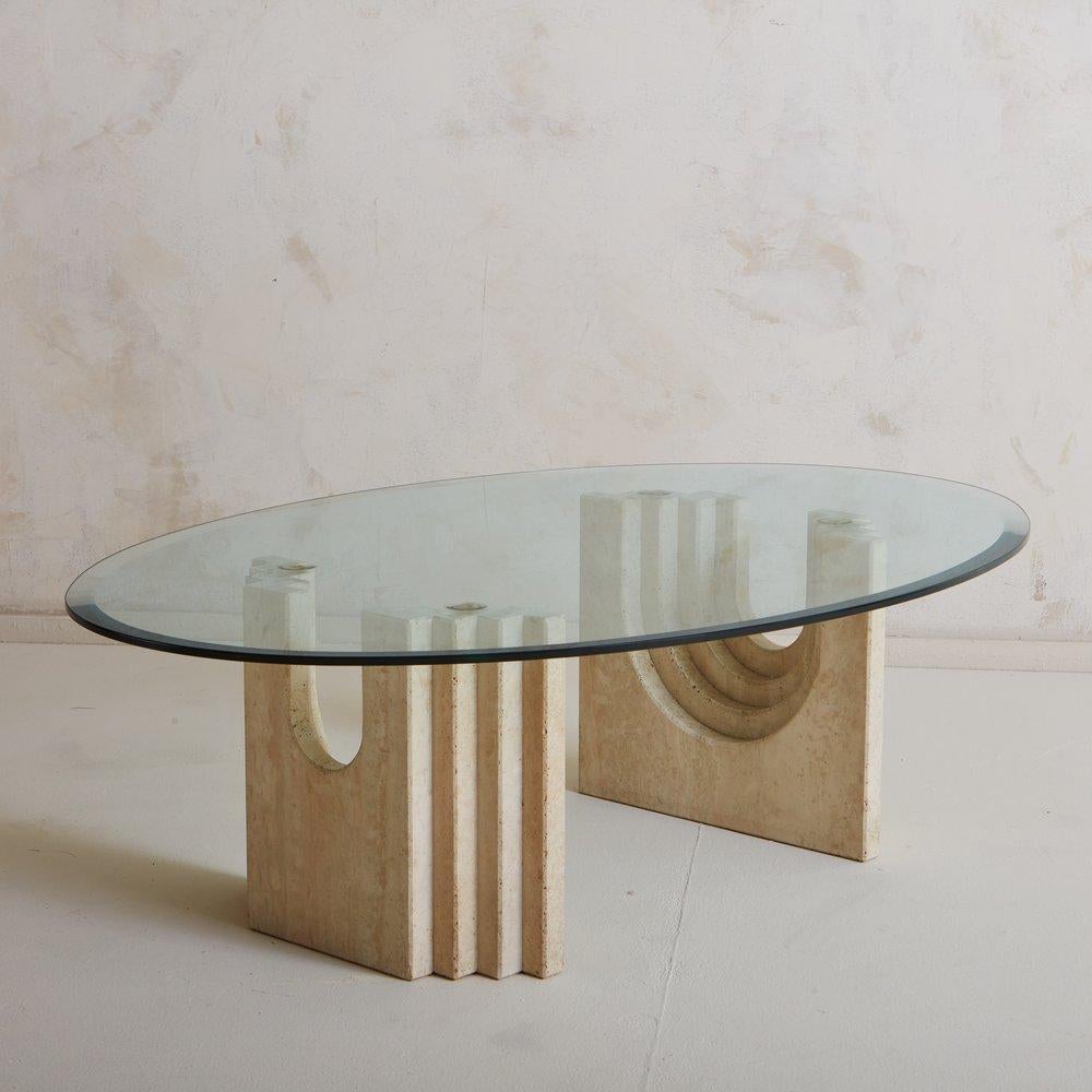A striking 1970s coffee table in the style of Carlo Scarpa. This table features an architectural base consisting of two travertine blocks with a graduated demilune cutout. It has an oval glass top with a beveled edge. Sourced in Italy, 1970s.