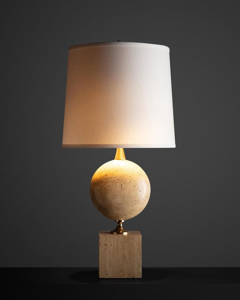 Cream colored travertine sole with a brass structure supporting a travertine sphere.