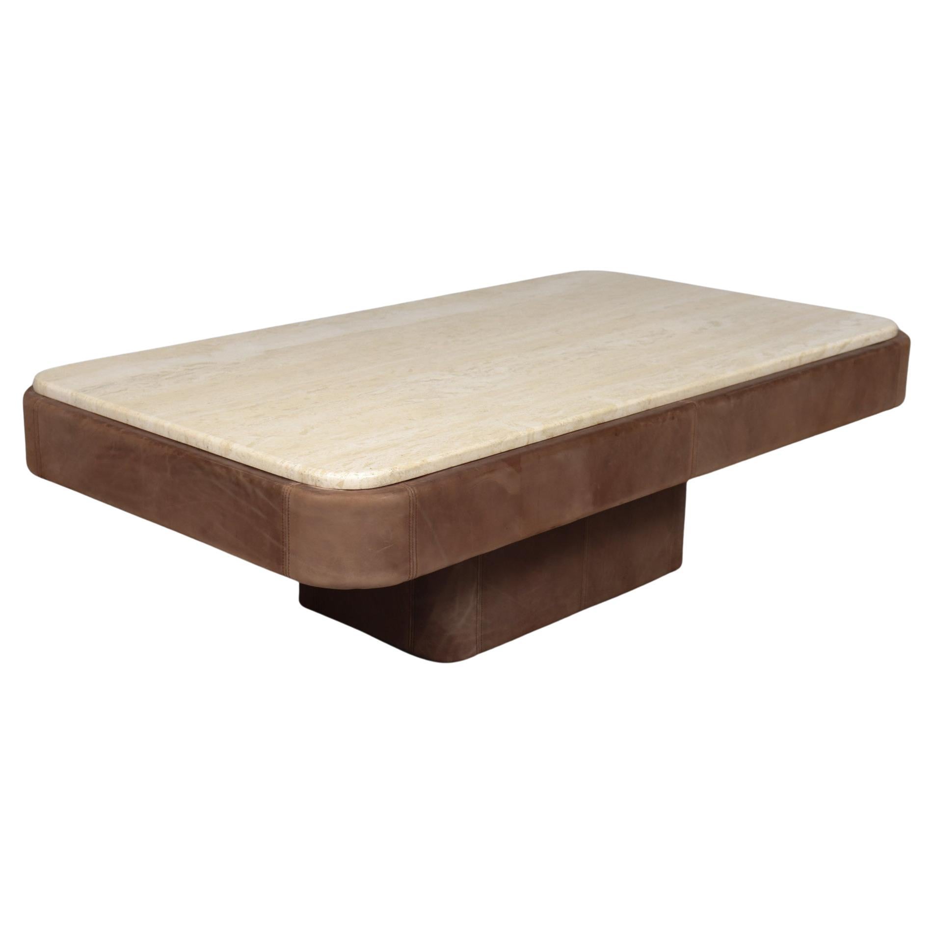 With this coffee table, the use of a wide variety of materials creates an impressive ambiance: with a beautiful ribbon of high-quality leather, the tabletop is covered all around. The top itself is made of travertine. The deep architecture
