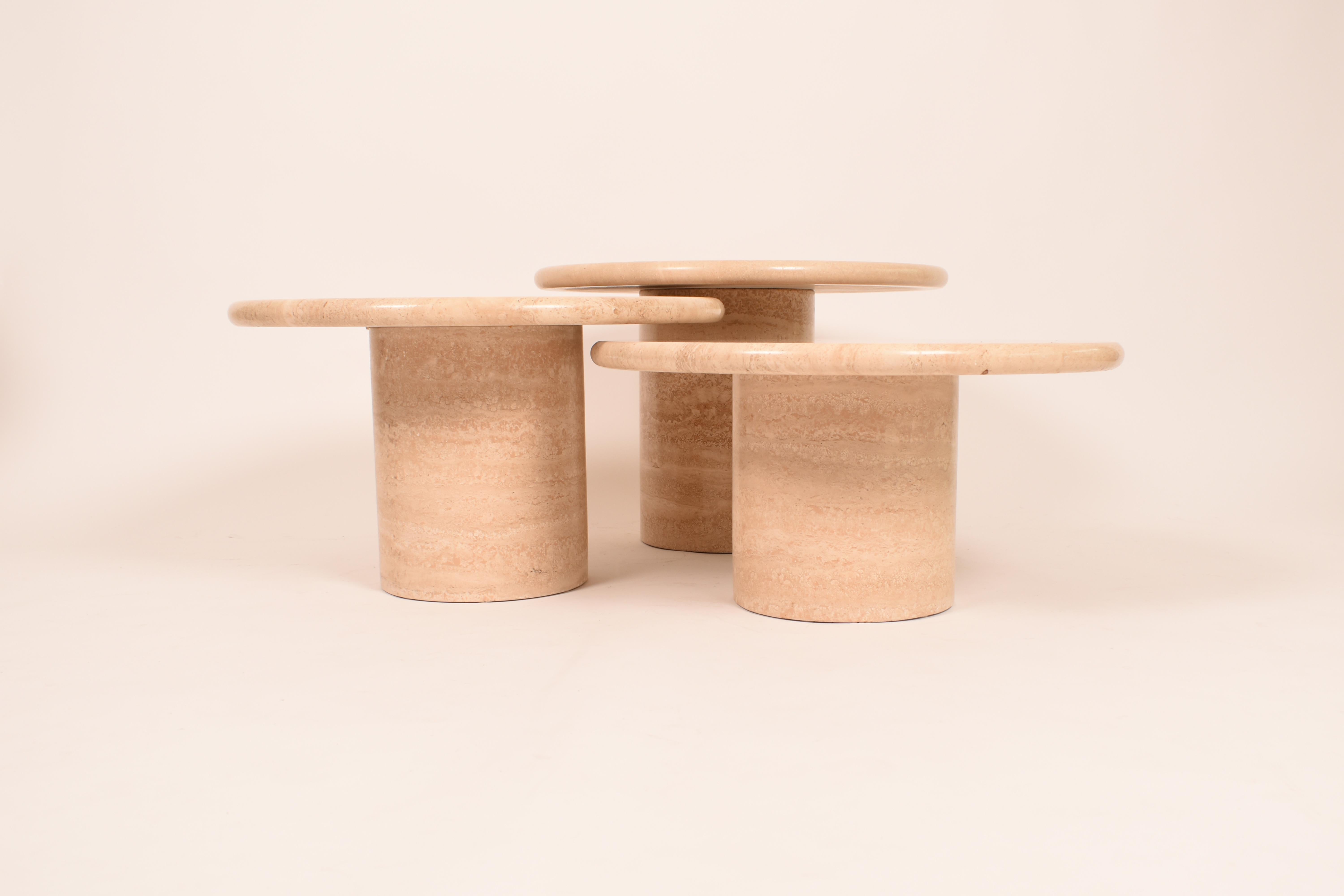 This set of three coffee tables is made of cream travertine, with a bonded surface finish, wich protects the stone from atmospheric dirt or liquid agressions.
The round, curved nose table tops are sitting on a hollowed central leg.
These legs have