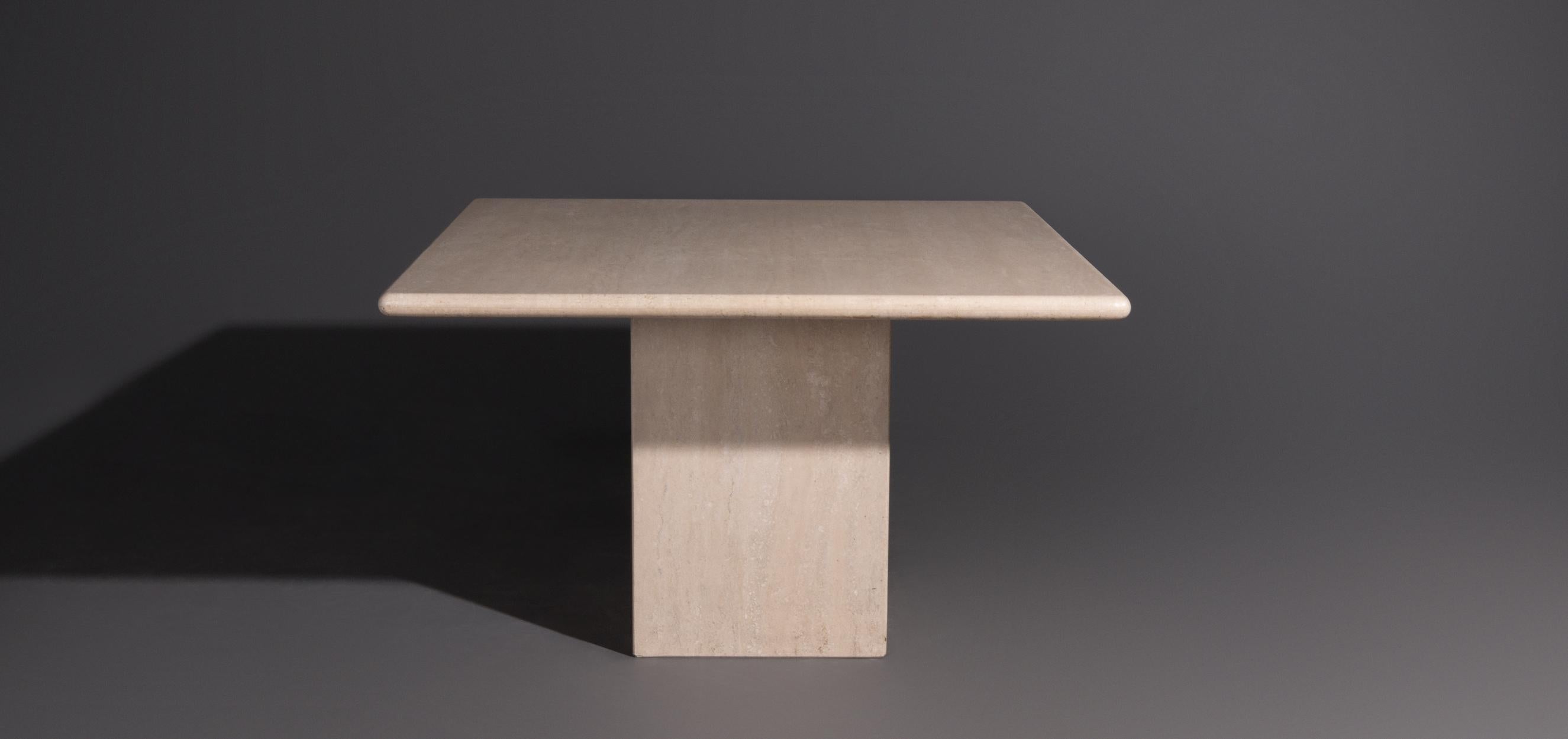Travertine dining table with a square top. This dining room table has a top with rounded edges. The table is made of travertine, a natural stone with a beautiful pattern. The travertine has a beige color. The leg is loose from the leaf, but because