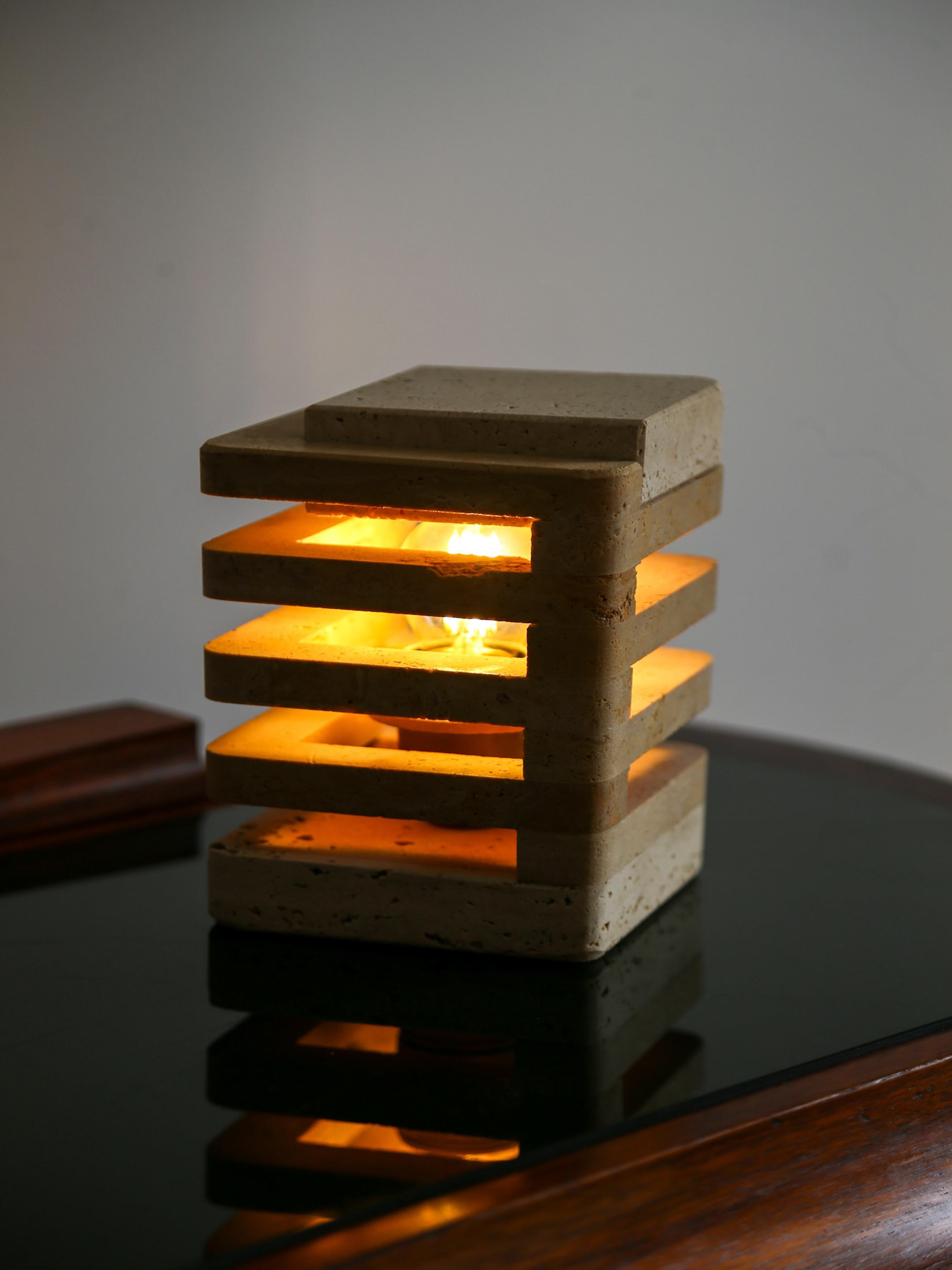 A striking architectural table lamp by Fratelli Mannelli, crafted in Italy during the 1970s from solid travertine. Characterised by its layered geometric form, the design features stacked, precisely carved slabs that allow warm light to diffuse