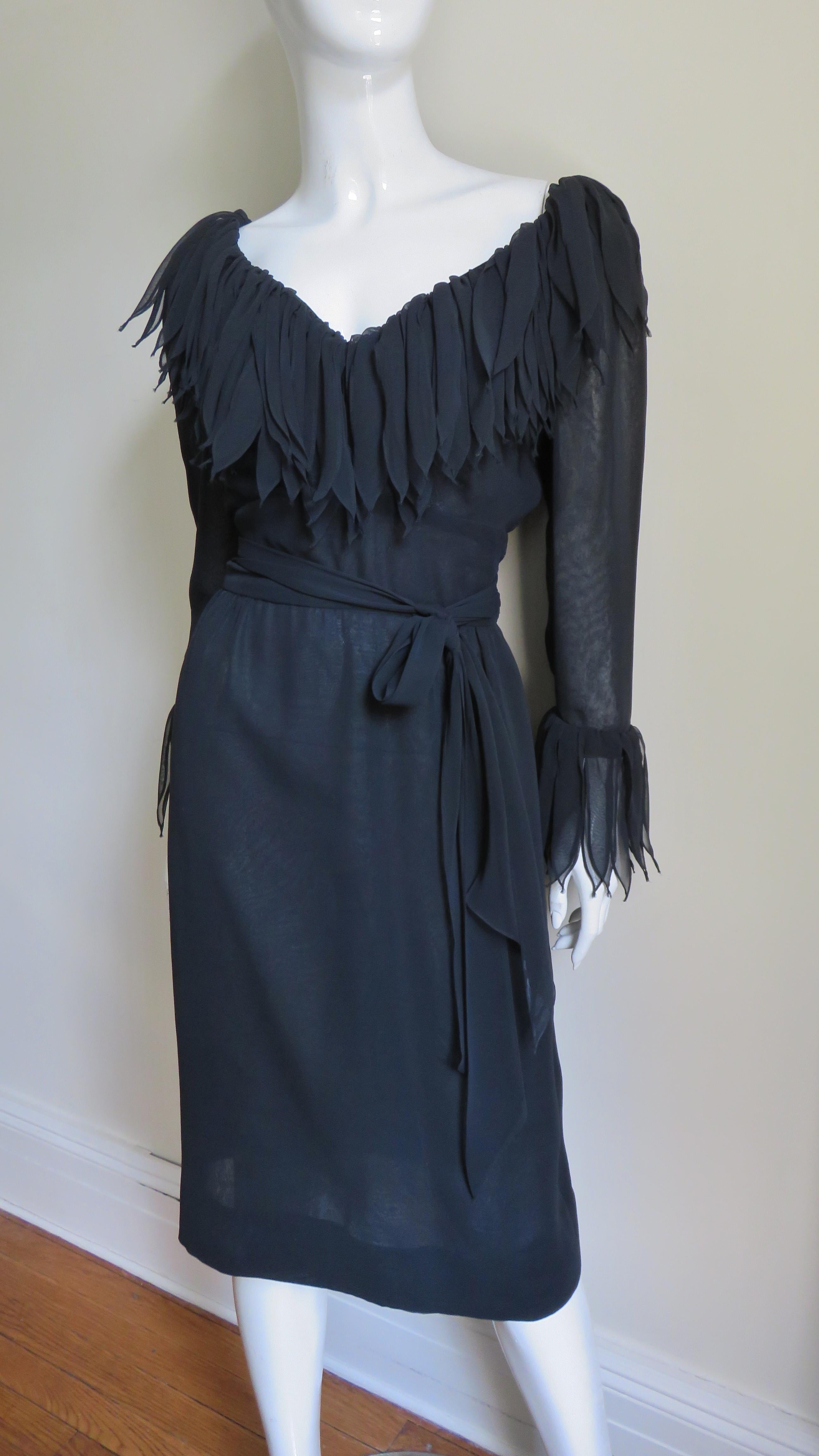 An incredible black silk dress by William Travilla.  It is semi fitted with a wrap tie belt at the waist, a V neckline and a straight skirt.  Around the neckline and cuffs there are layers of 7