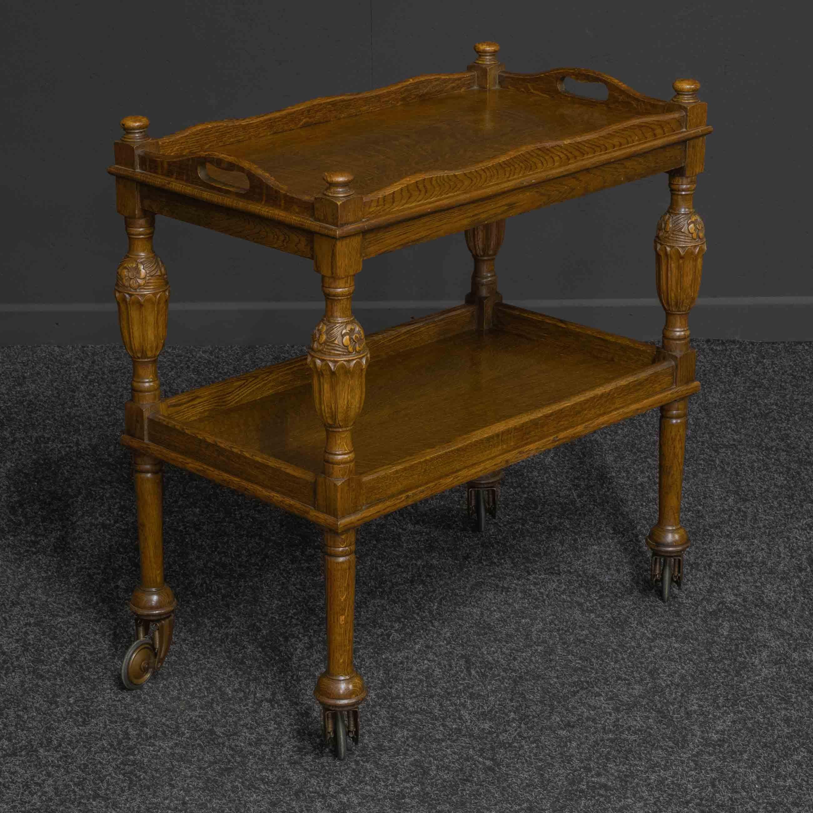 A superb quality oak tea trolley with well carved baluster central supports leading down to turned legs which terminate on the original and rare 'suspension' castors. The quarter veneered tops show beautiful figuring, the upper one a two handled