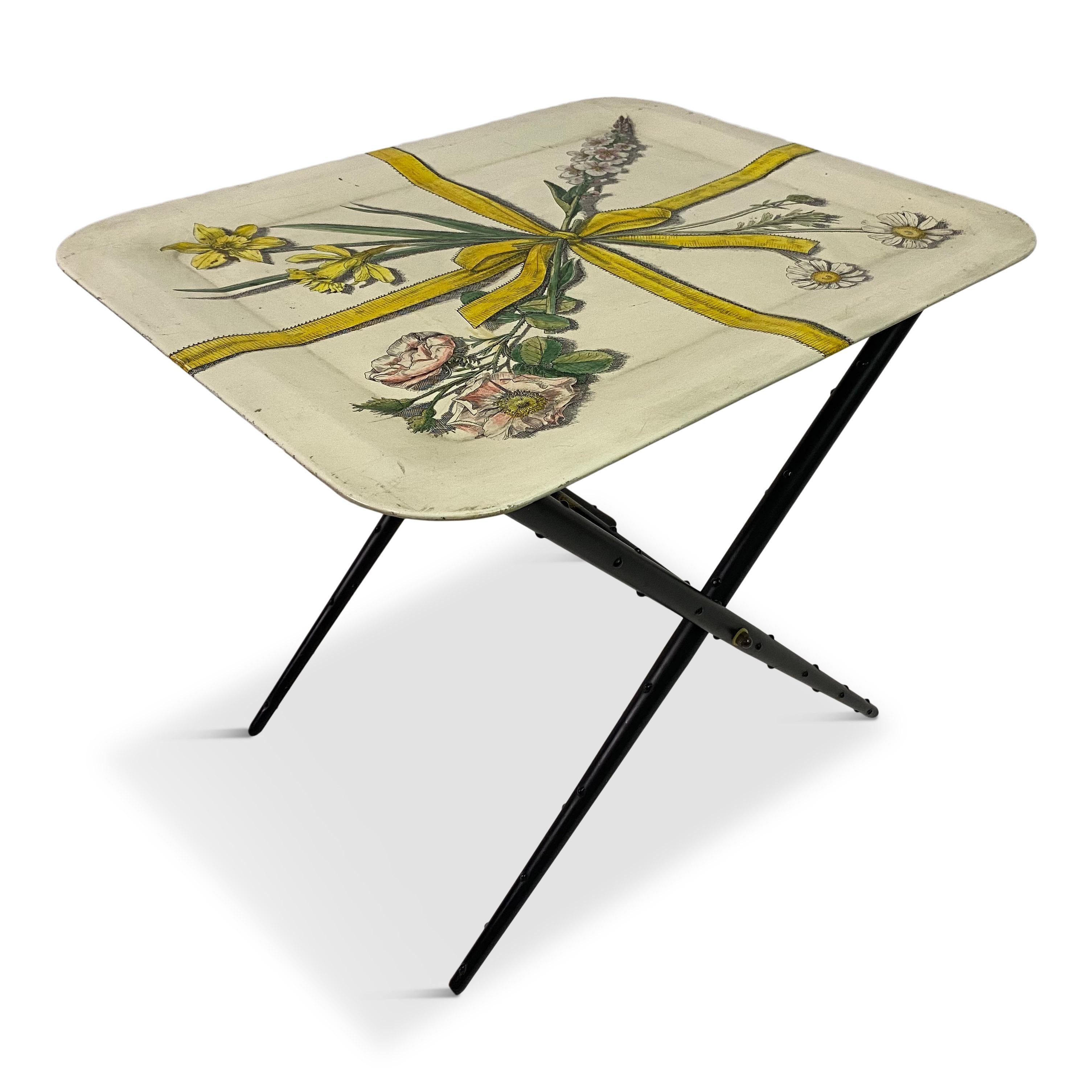 Tray table

By Fornasetti Milano

Lithographically decorated

Enamelled steel

Flower and bow images

Folding black stand

Tray and stand with Fornasetti labels

Italy 1960s.