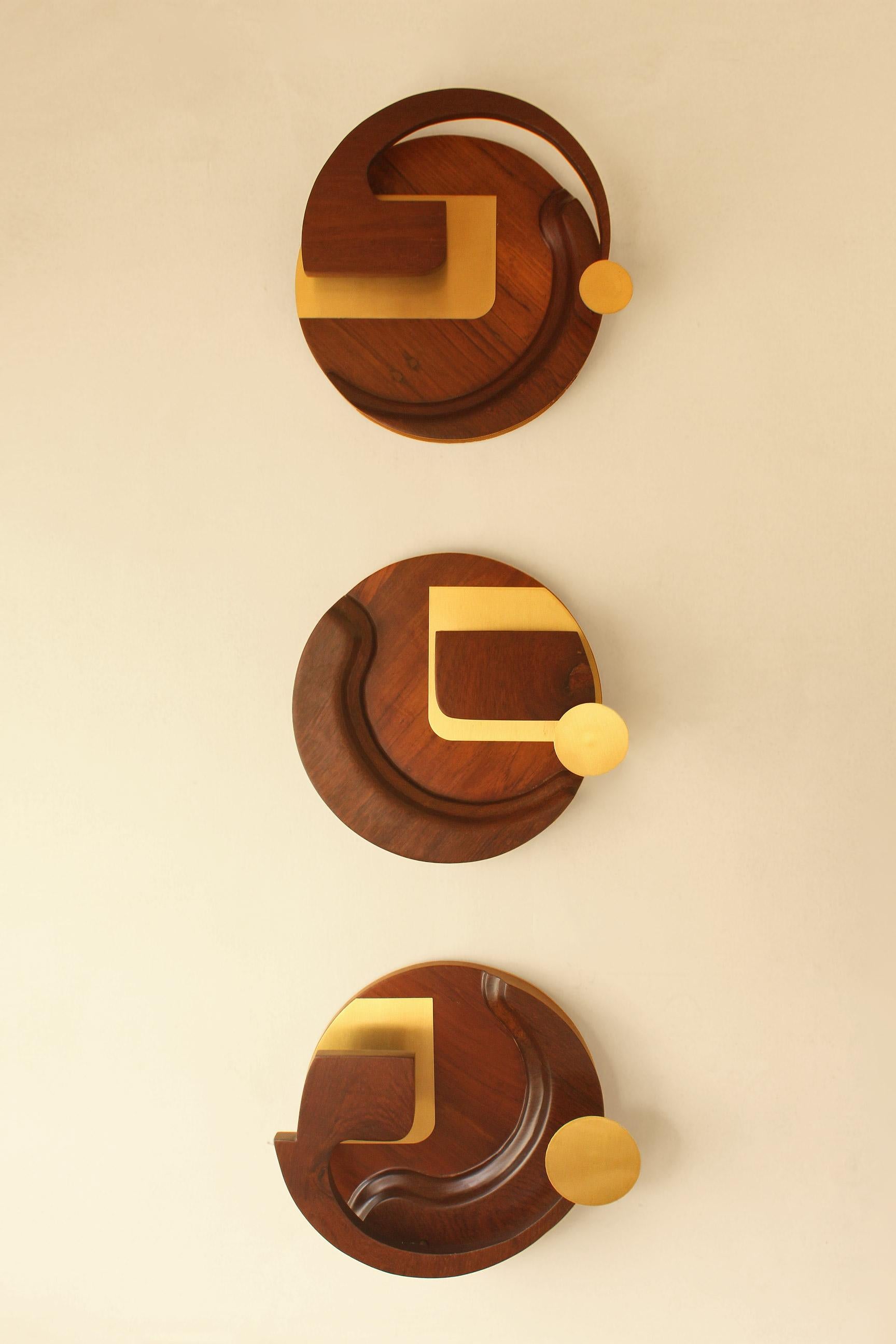 Traya Wall Lamp by Studio Indigene
Dimensions: D 30.48 x W 30.48 x H 7.62 cm
Materials: Teak Wood & Brass. 
Colors Brown, Natural Wooden Finish.

Traya, a 3-piece wall mural with lights, is a fluid abstract composition, played out in 3 circles, and